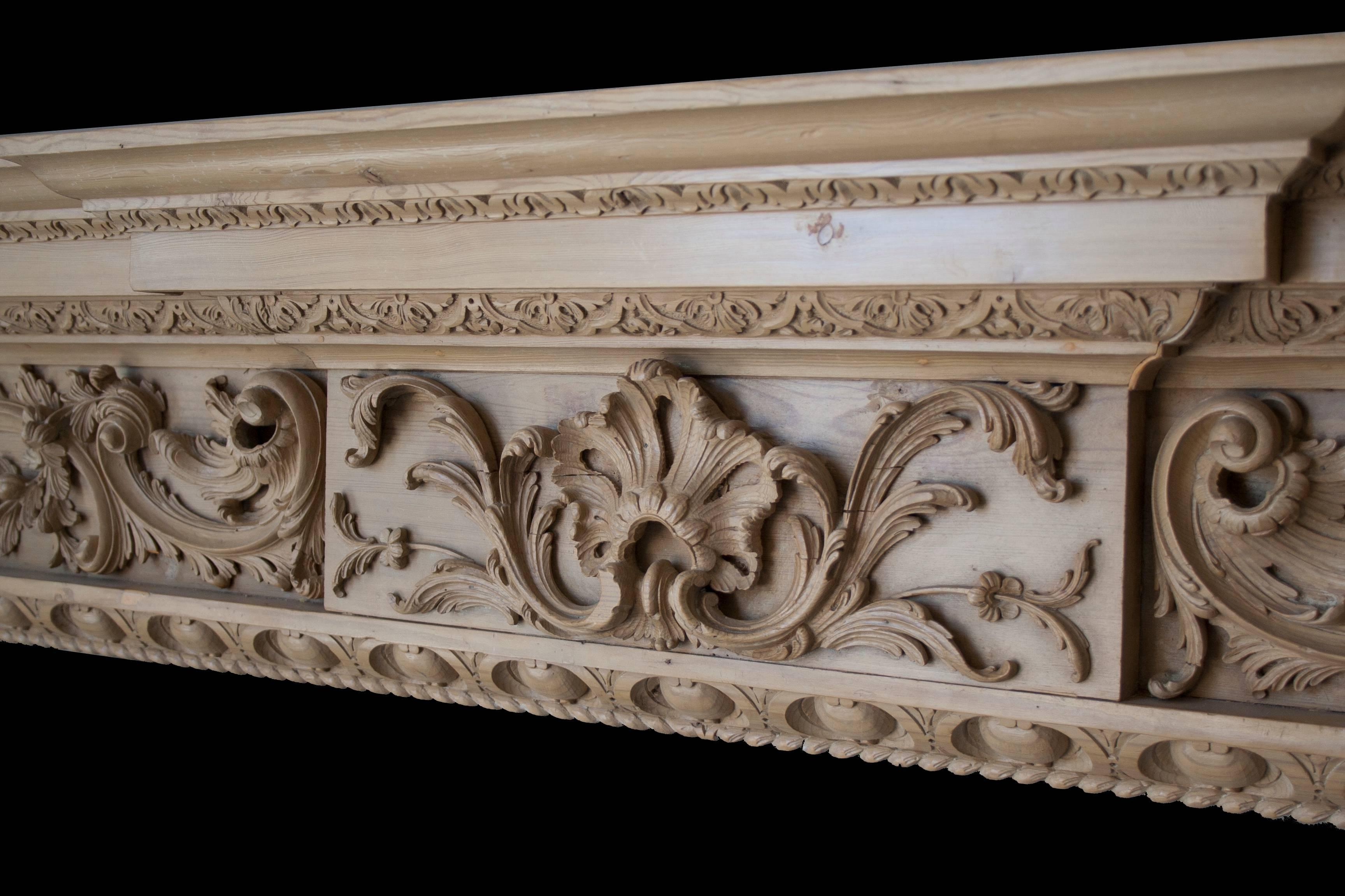 A fine Rococo style antique pine fireplace surround in the Georgian manner, with a richly carved floral frieze centred by a large shell cartouche and with lambs tongue, egg and dart undershelf carving and acanthus leaf detail around the opening. We