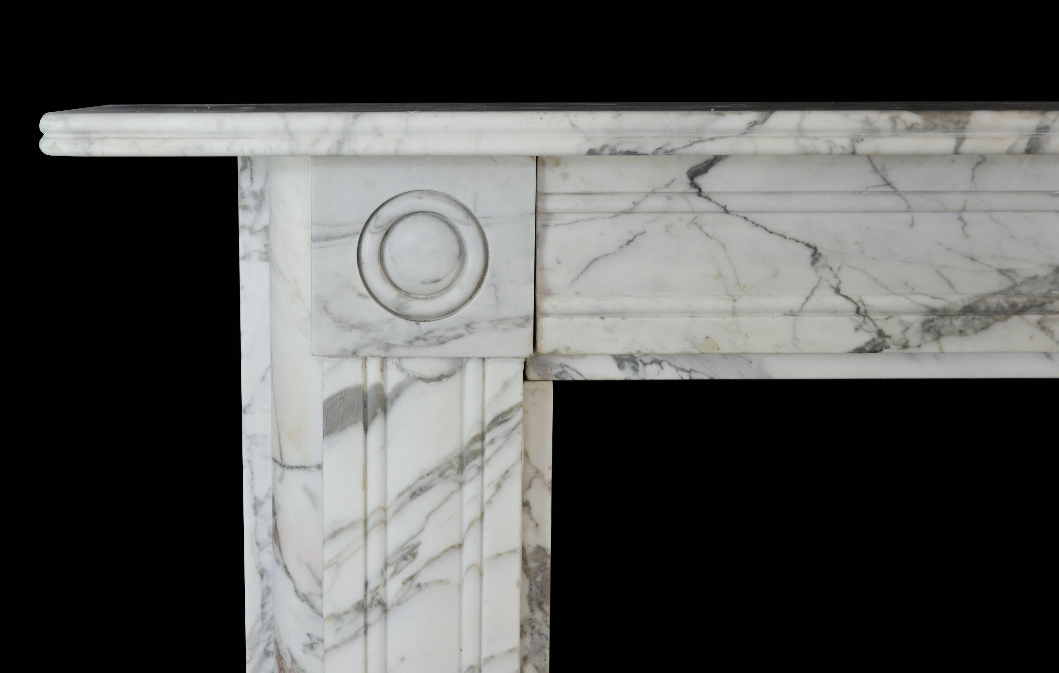 A Regency mantelpiece in Carrara marble with molded cushion panel jambs terminating beneath bullseye corner blocks, confirming frieze panels flanking a center tablet of similar design and a reeded mantel shelf, circa 1820.

Opening dimensions: 36