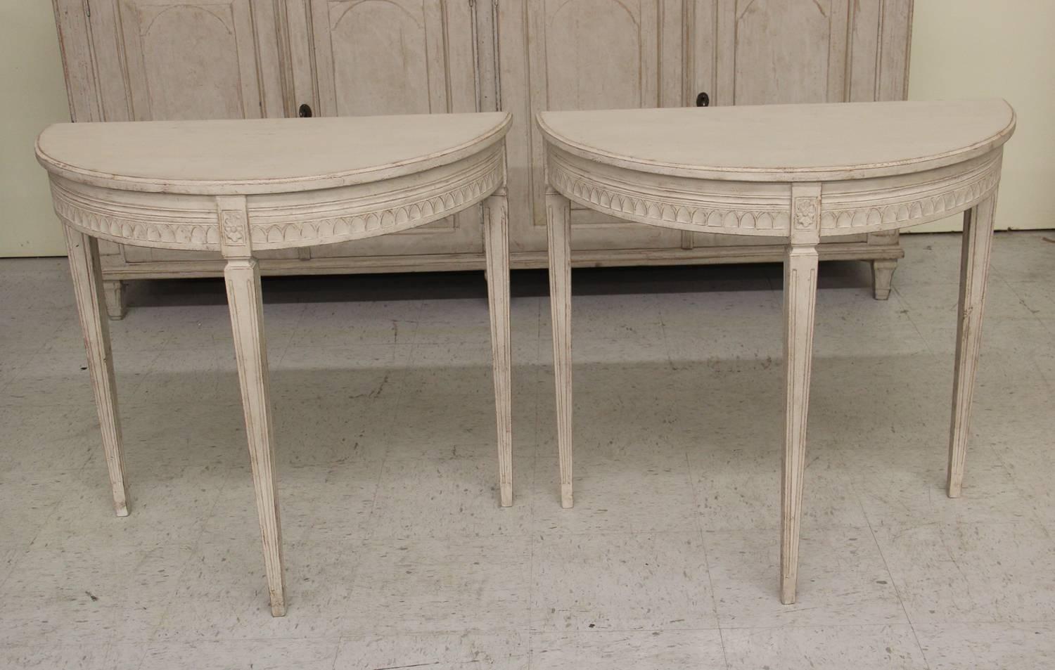 A pair of Swedish Gustavian style small demilune console tables from the 19th century. The tables feature carved rosettes with lamb's tongue carving on the apron; raised on square, tapered and fluted legs.