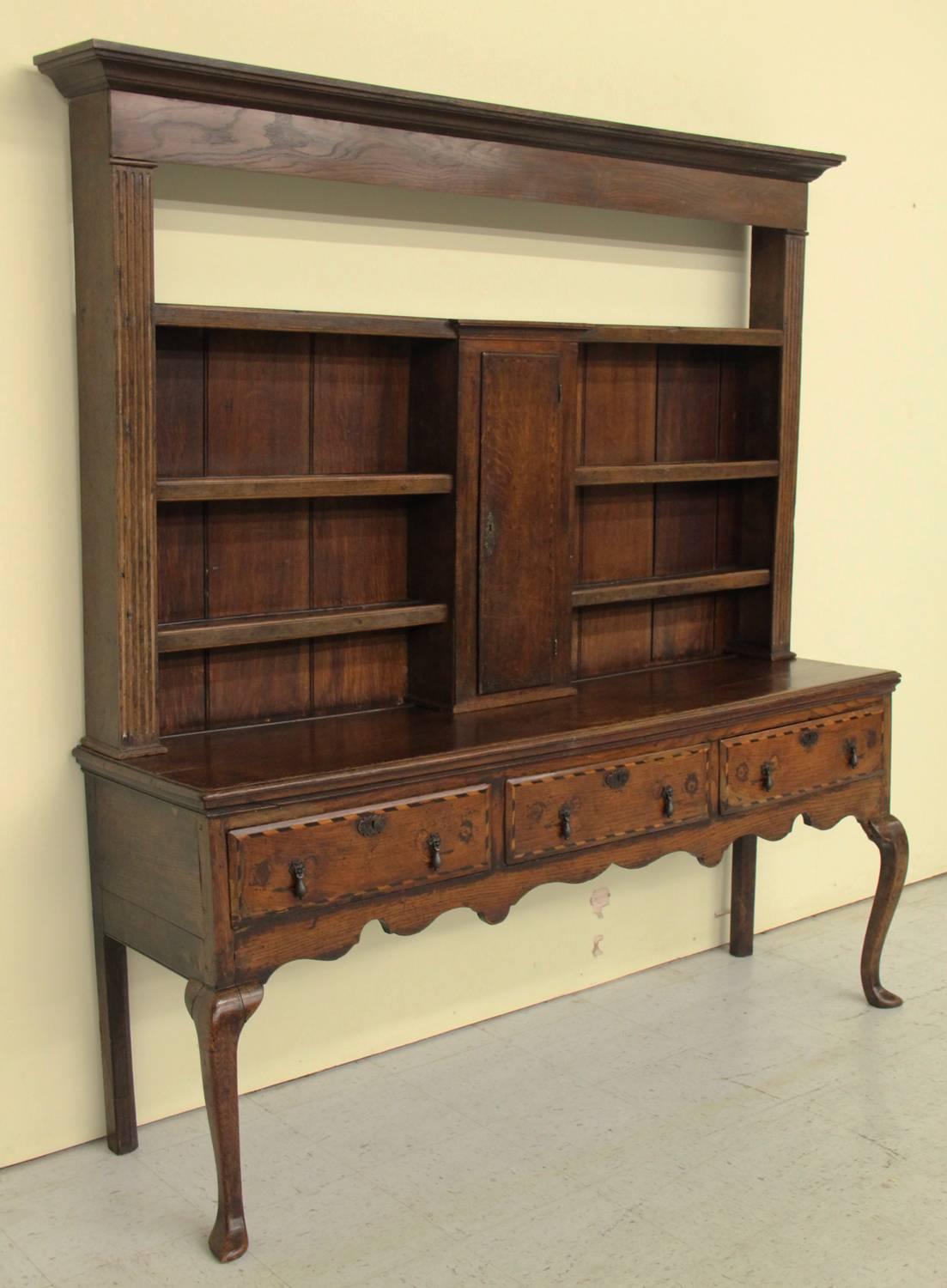A late 18th century two-part English oak Welsh dresser server or buffet with an exceptional patina from the Georgian period. The upper section has four shelves and a central cupboard door. The lower section has a scalloped apron and three drawers