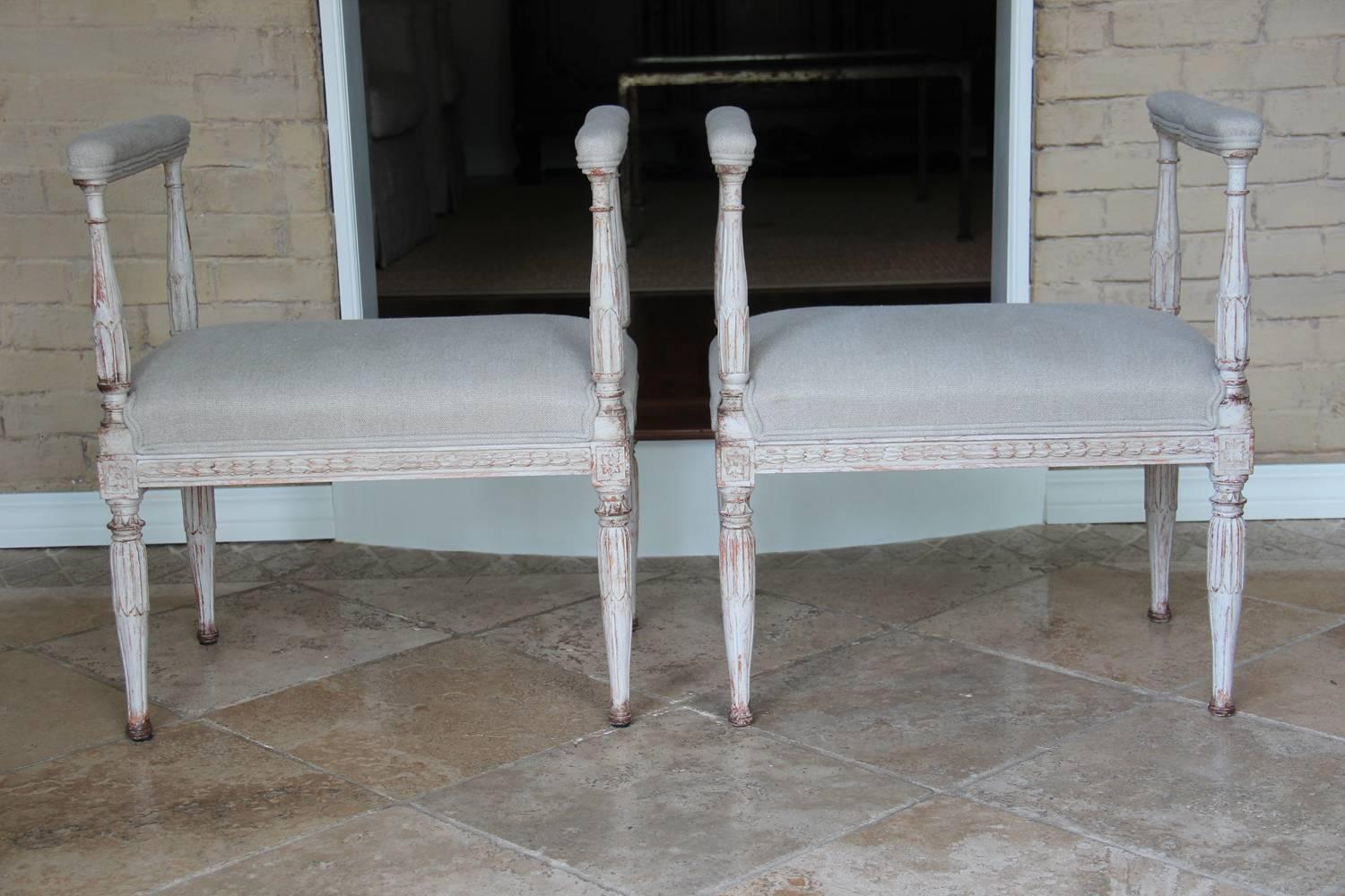 A rare pair of 19th century Swedish Gustavian window seat stools with padded armrests, newly upholstered in Fine de Le Cuona Belgian linen, Urban Linen, color stone. The seat frame features beautifully carved acanthus leaves that are repeated on the