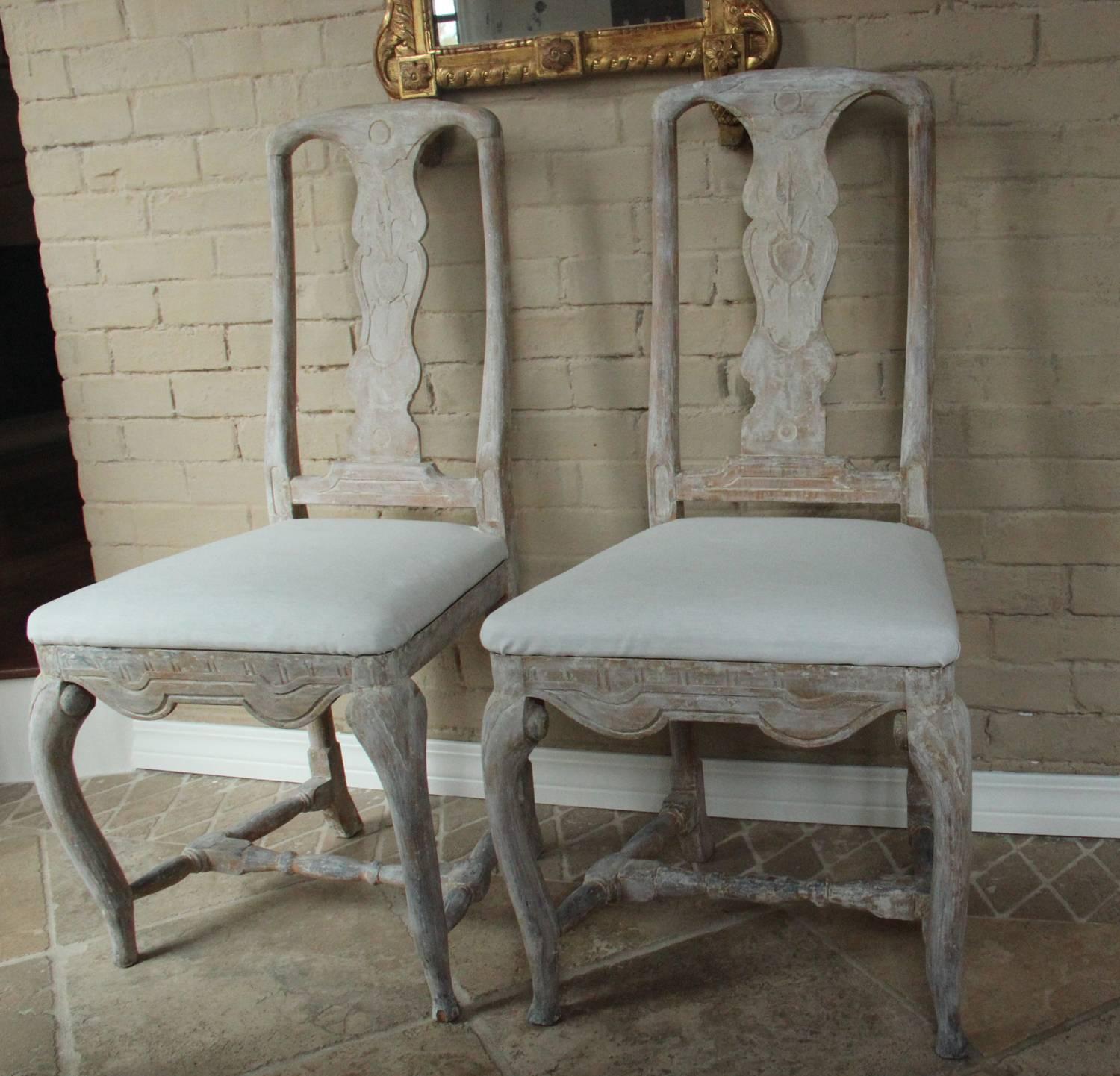 A stunning pair of 18th century, Swedish dining chairs from the Rococo period with splat backs carved with a family crest, carved and shaped seat rail, refined cabriole legs, H-shaped stretcher and slip seats. Beautifully proportioned and hand