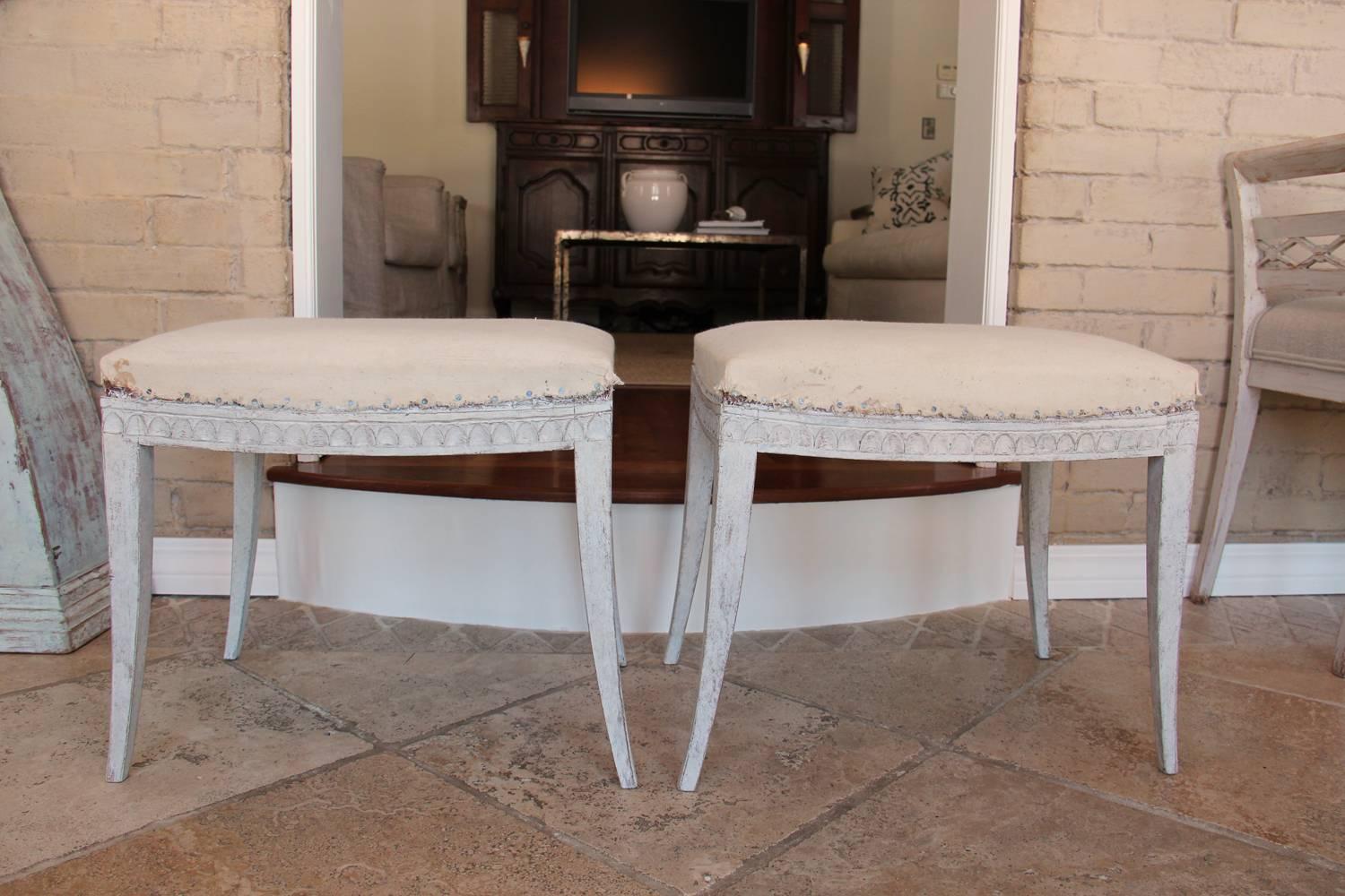 A pair of 19th century Swedish stools from the Gustavian period with original horse hair seats. Chalky Gustavian grey-white paint on a carved lamb's tongue frame and raised upon slender saber legs.