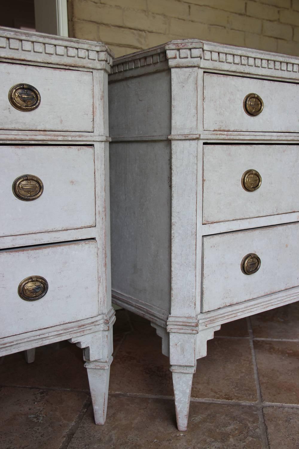 An elegant neoclasical pair of Swedish painted commodes in the Gustavian Style. Each chest has three drawers, brass hardware, and original locks and keys. The corner posts are canted. The shaped top is framed by dentil molding and the chests rest