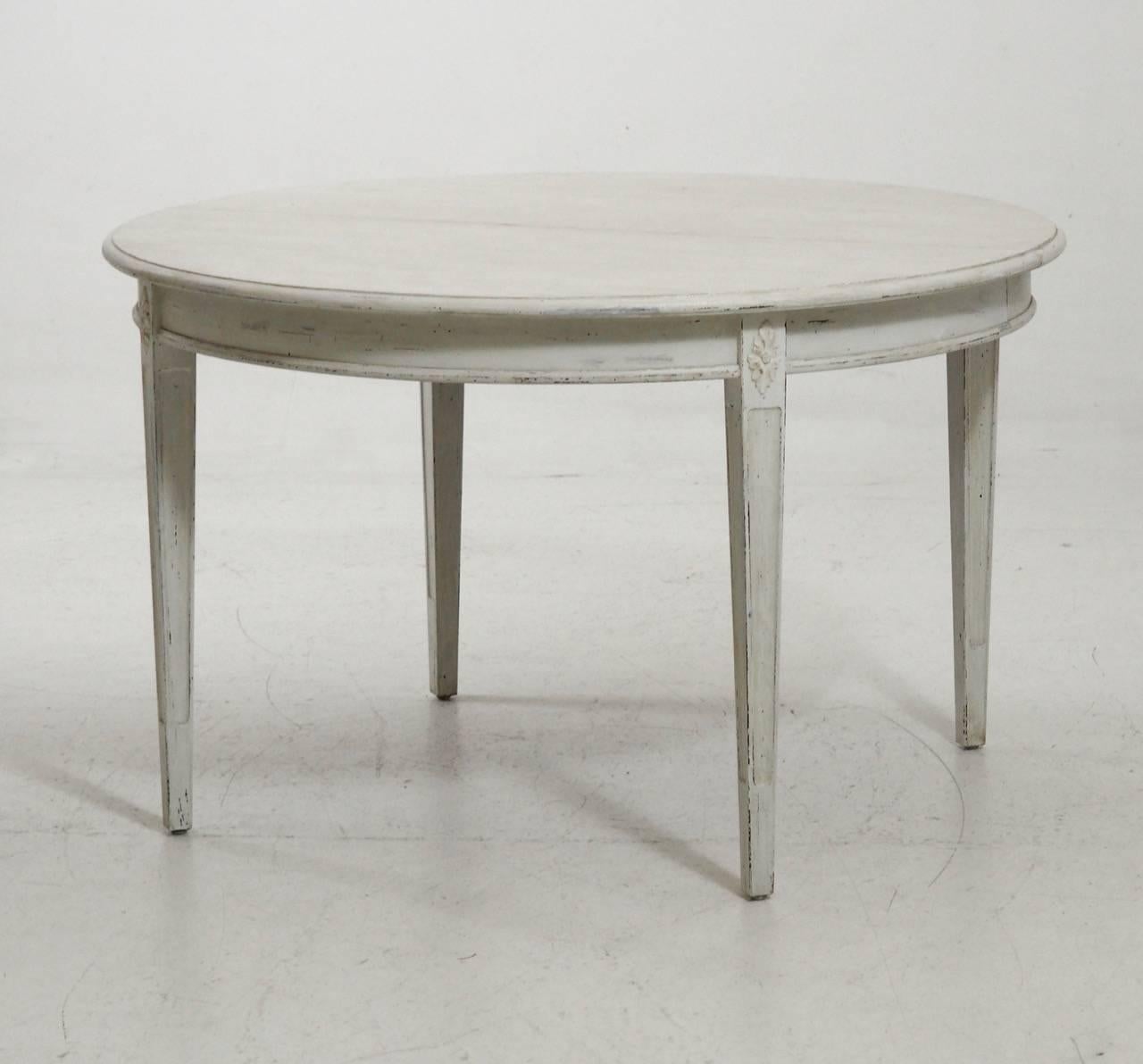 A beautiful Swedish three-leaf oval dining table in the Gustavian style with an antique white patina. This is a charming and versatile table that can extend with one, two, or three leaves. The table rests upon square, tapered, and fluted legs and