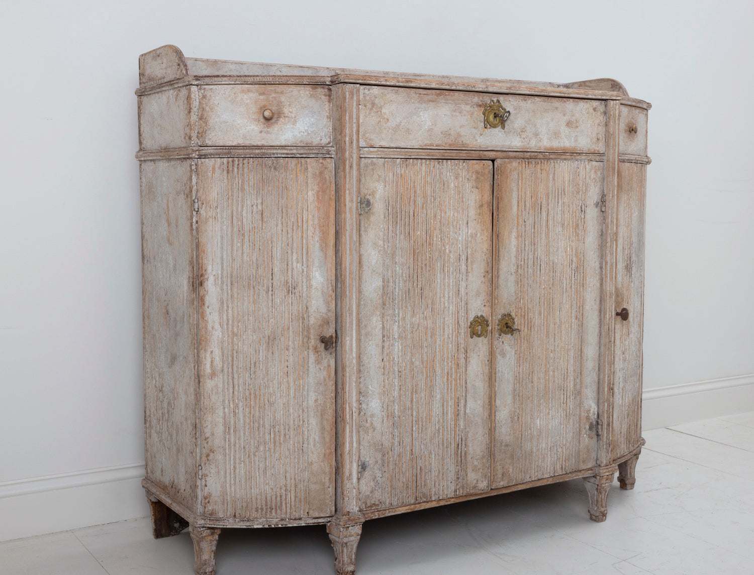 A Swedish demilune sideboard or server from the Gustavian period. The patina is a beautiful soft gray with natural wood showing through in areas. The buffet has three drawers. Four reeded doors open to reveal one center shelf and two side shelves,