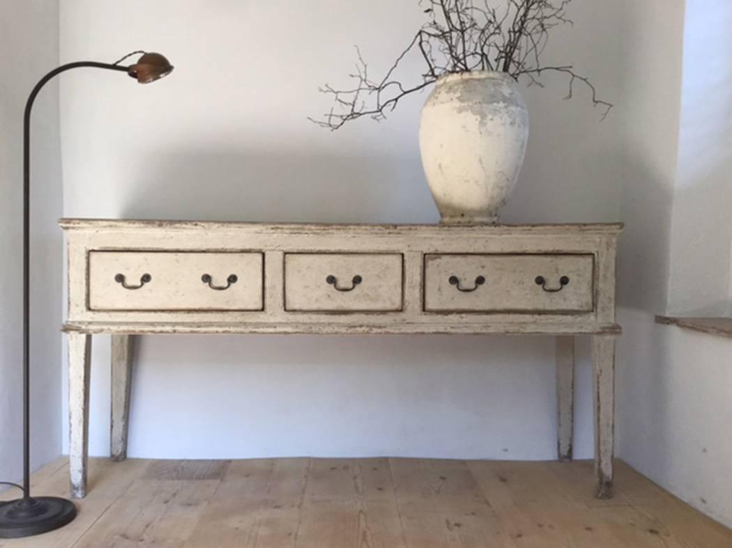 A very charming English country house credenza in a pale off-white patina with three drawers from the 19th century.  This server would make a lovely console table in an entry hall.   It would also suit a kitchen or dining room as a unique sideboard