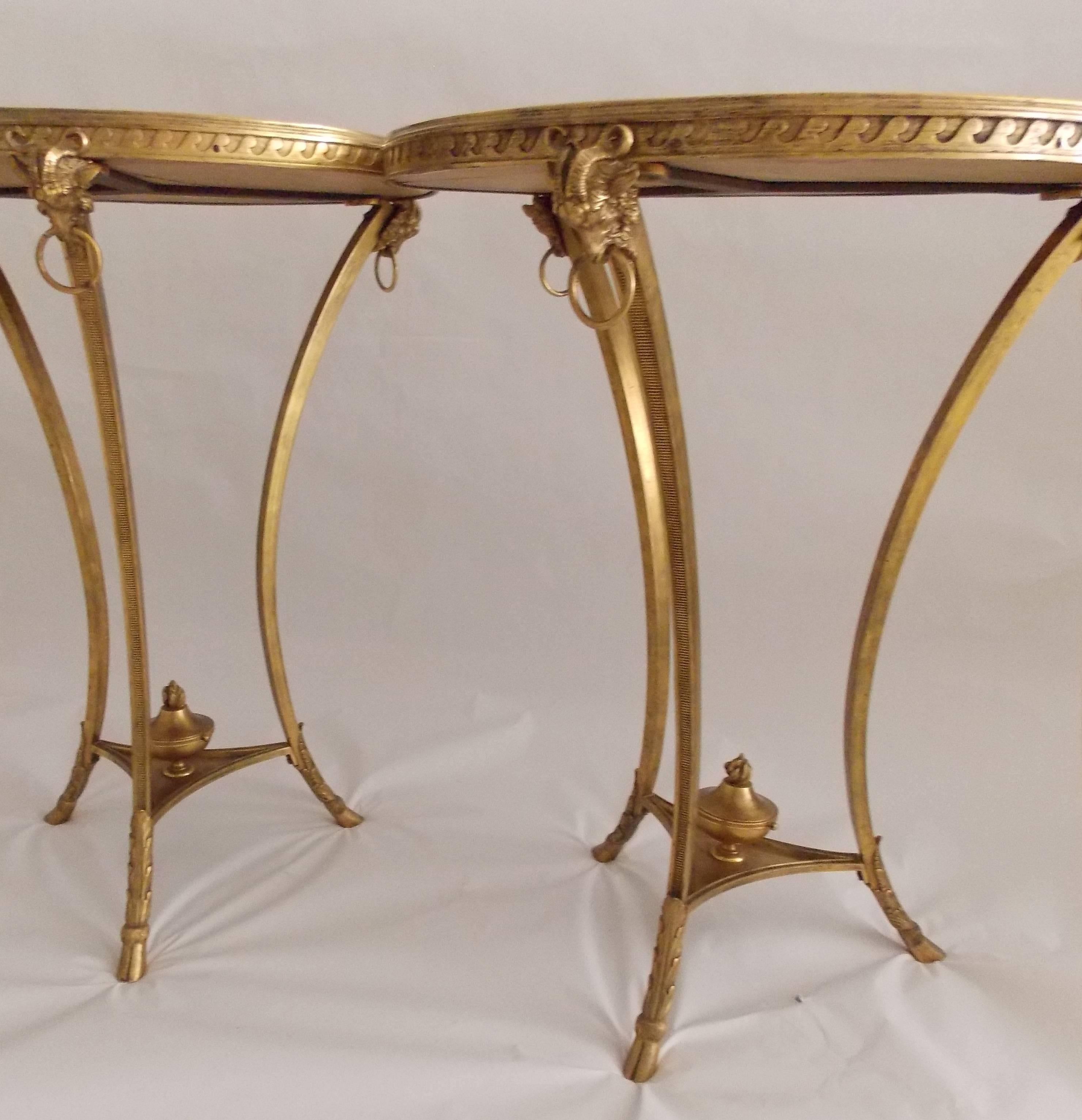 An exquisite, transitional pair of French Neoclassical style gilt bronze Gueridon tables with specimen bois de rose marble tops and ormolu ram's head and flaming urn detail. Each Gueridon is accented with acanthus leaves at the base and ends with a