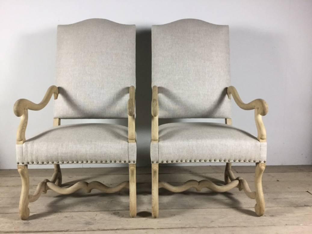 A large pair of French Os de Mouton armchairs, so named because the legs resemble that of a lamb's leg. These charming, bleached oak chairs have been newly upholstered in natural linen and finished with decorative nailheads.