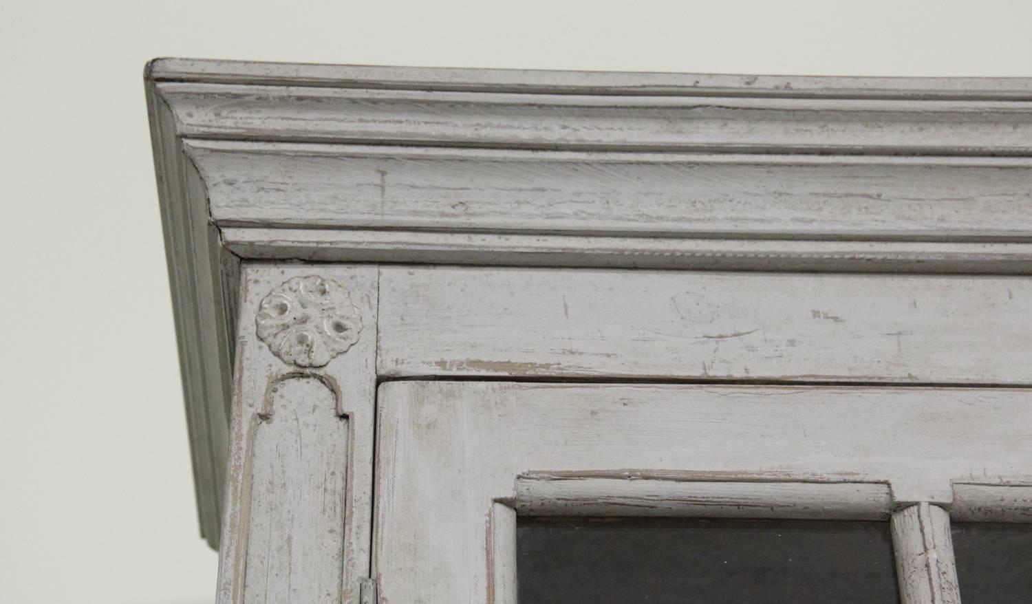 A Swedish late Gustavian four-door painted vitrine cabinet from the 19th century. This classically designed piece is made in two parts. The upper section features three shelves behind original glass doors. The top of the lower section is framed by