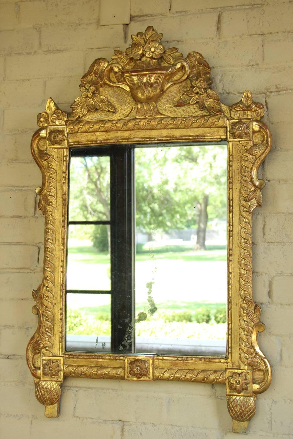 A richly carved 18th century French Louis Seize period original giltwood mirror with floral and urn motif and mercury plate. The carved crest features an urn filled with a bouquet of trailing flowers. The floral and leaf motif continues along the