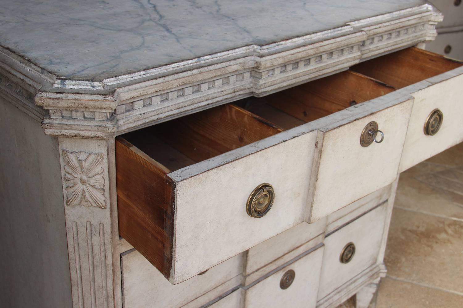 A beautiful Swedish Gustavian breakfront chest from the 19th century with a hand-painted marbleized top, framed by dentil molding. There are three drawers with brass hardware and the top drawer is divided into three sections. The corner posts are