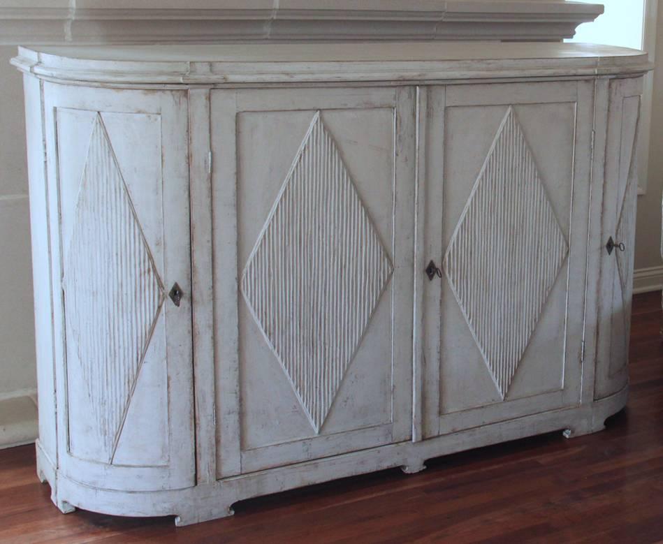 A Swedish demilune buffet or server from northern Sweden where the Gustavian style survived longer. The patina is a beautiful chalky old white with gray and cream tones and wood showing through in areas. There are three interior shelves; the top