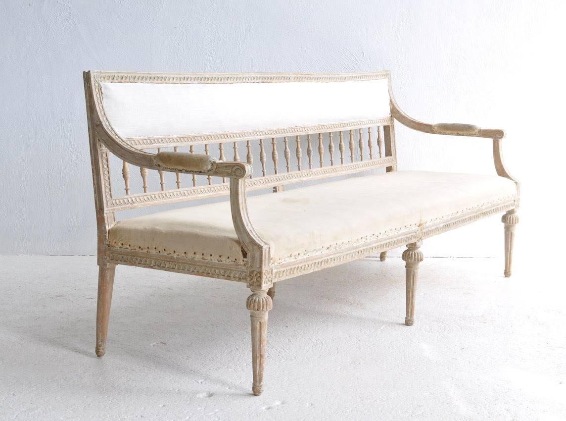 A classic Gustavian period sofa from Lindome, Sweden that has been hand-scraped down to the original creamy white paint. The back and seat frame are adorned with a carved egg and dart pattern. There are carved rosettes at each corner post and the