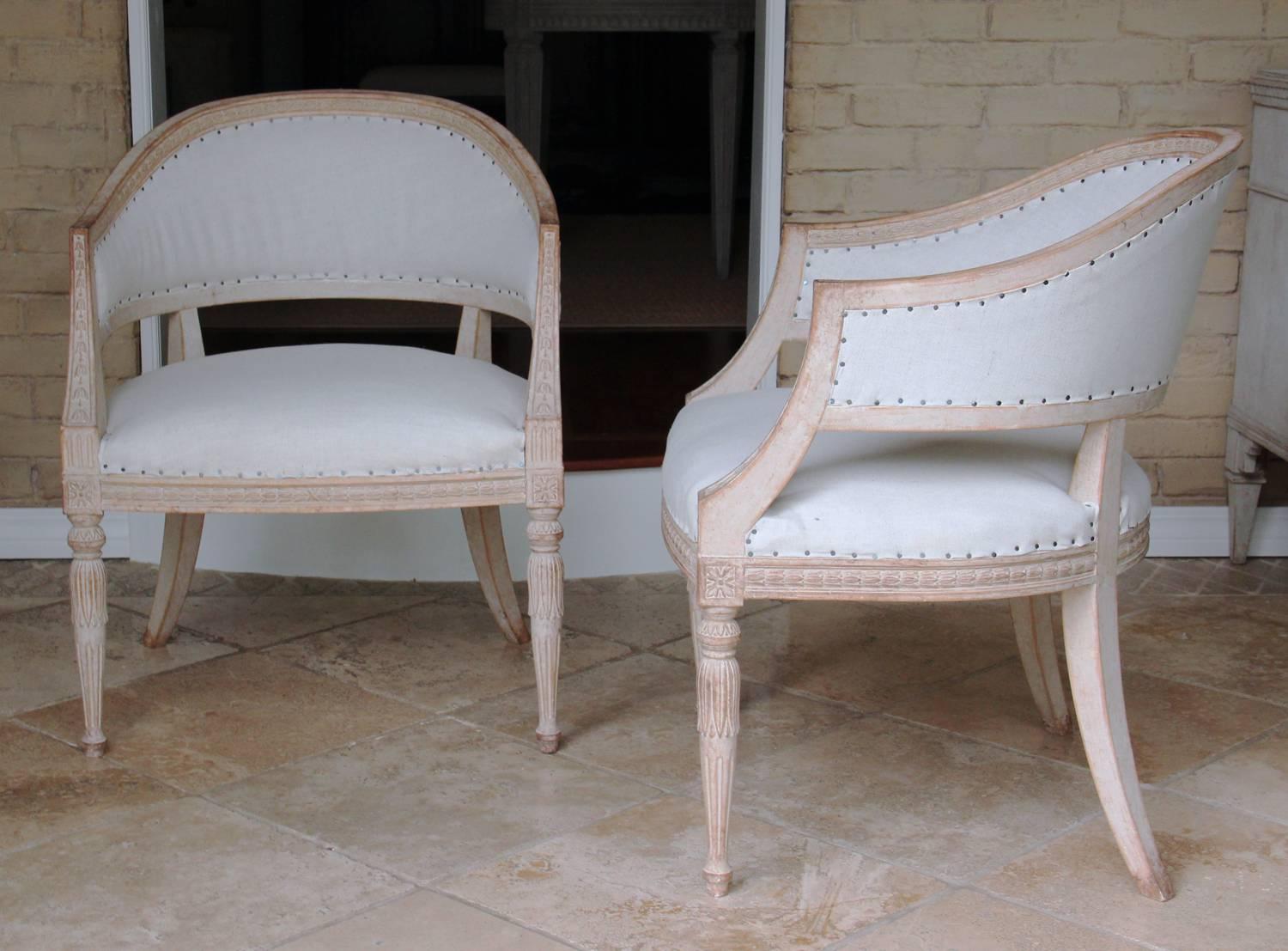 A pair of Swedish armchairs in the Gustavian style with barrel backs. These comfortable chairs have been newly upholstered in linen. There is laurel leaf and bell flower carved molding along the back and seat frame with rosettes on each corner post.