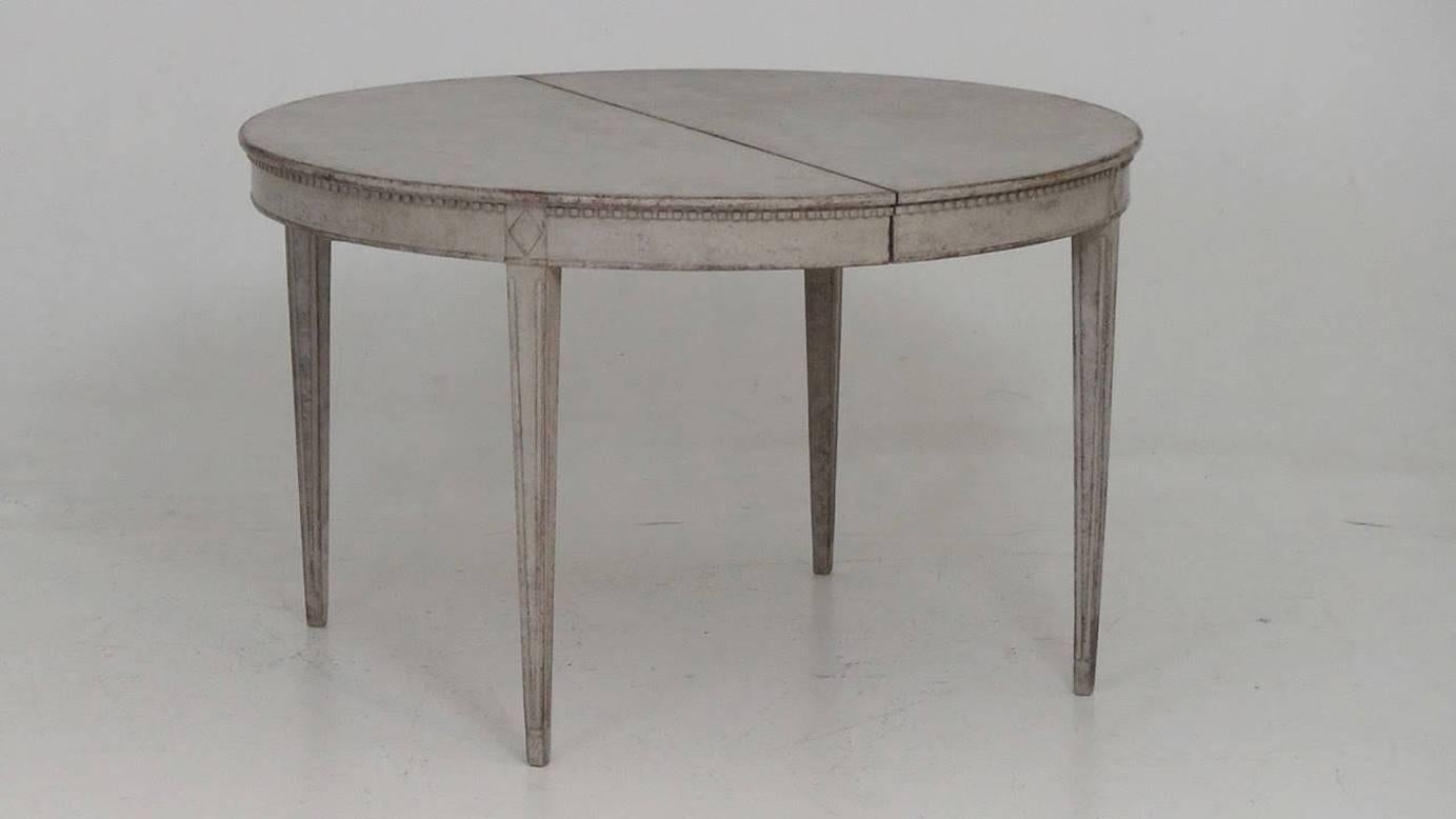 A beautiful Swedish Gustavian style oval dining table with two leaves, circa 1910. This is a charming and versatile table that can extend with one or two leaves. There is carved dentil molding around the apron and the table rests upon square,