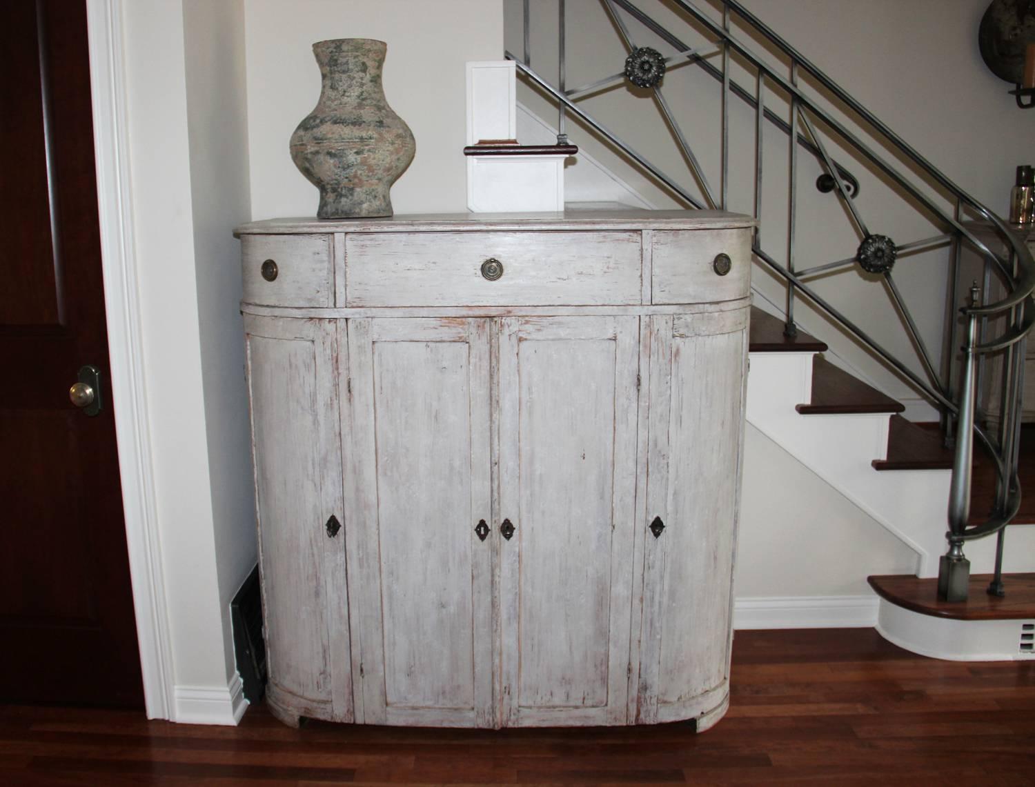 A Swedish demilune sideboard or server in original paint from the Gustavian period.  The patina is a beautiful chalky old white with gray undertones and wood showing through in areas. The buffet has three drawers and four doors. The center section