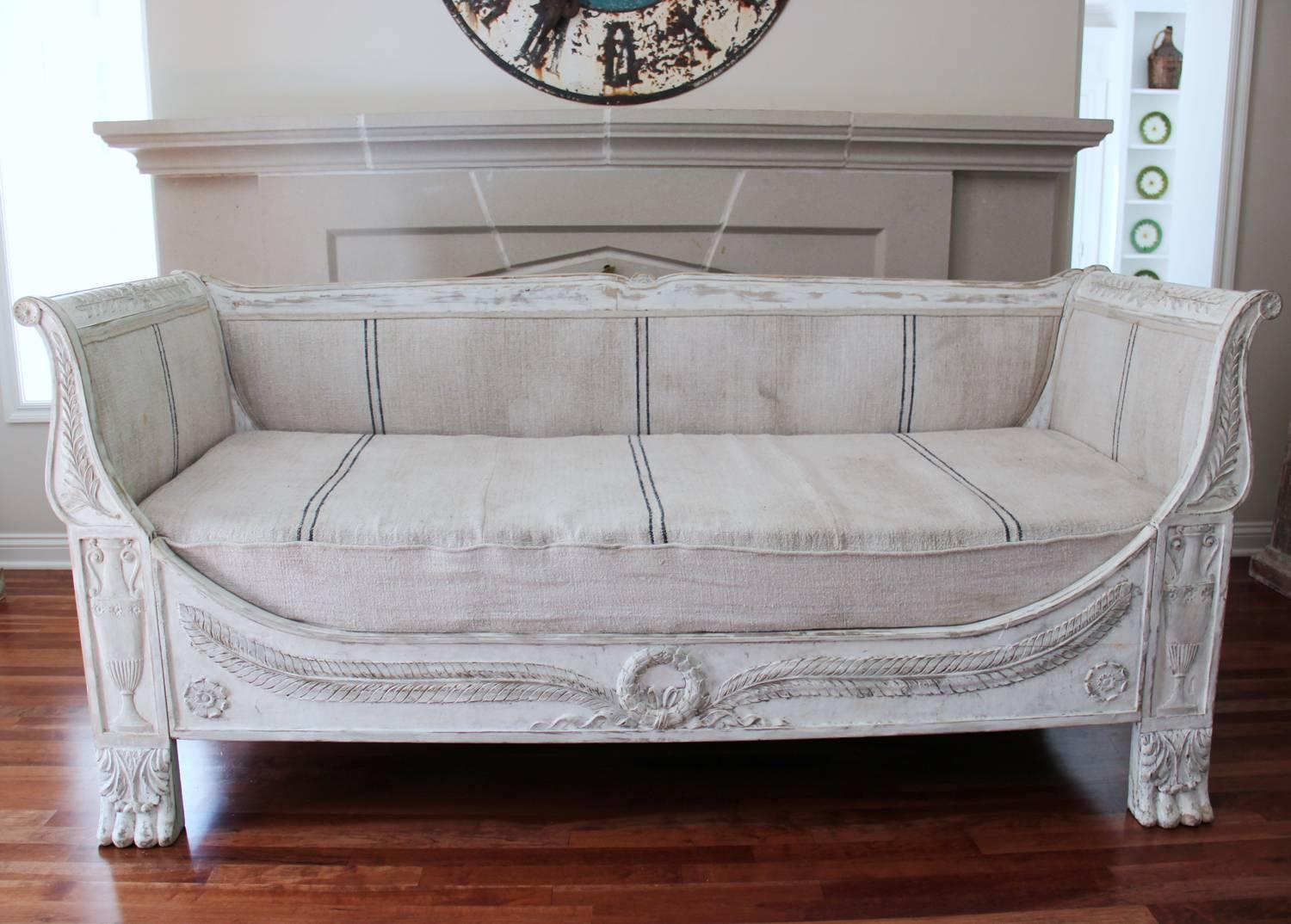 An early 19th century, richly carved, French daybed or settee from the Empire period with a beautiful painted white patina. This sofa sits comfortably, with a soft, yet firm seat. It has been newly upholstered in fine antique French linen. Measures: