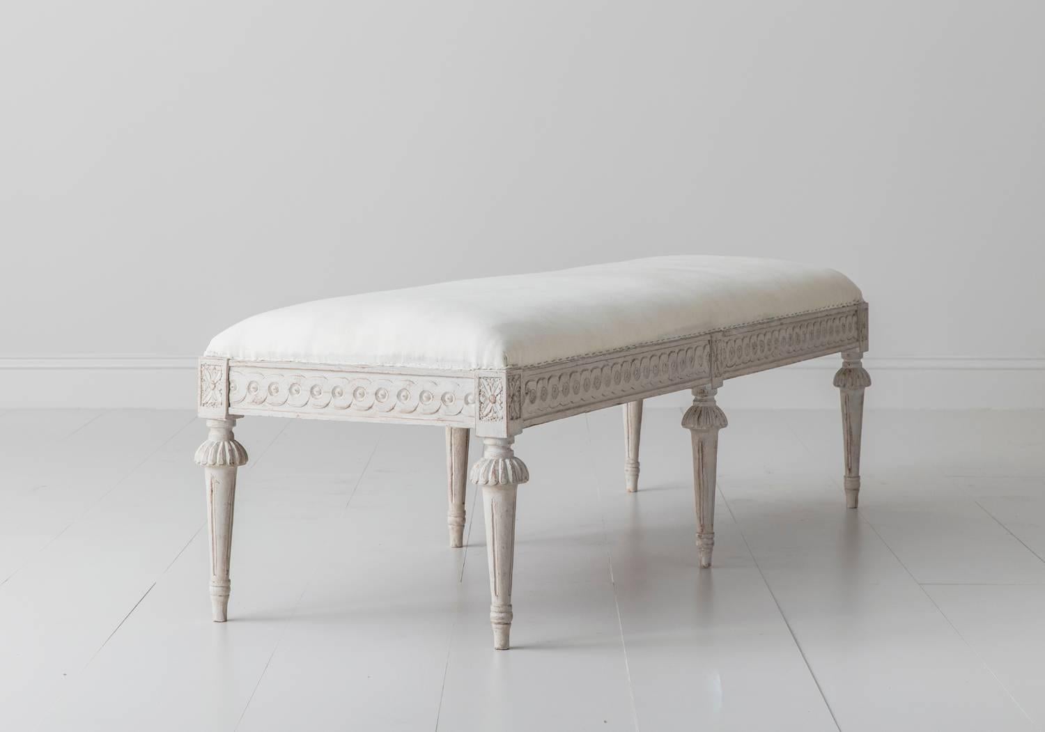 There is also a 'sister' bench available. Please inquire for details. This is a richly carved 19th century Swedish painted long bench in the Gustavian style. There is a carved guilloche pattern on the seat frame and carved rosettes above fluted,
