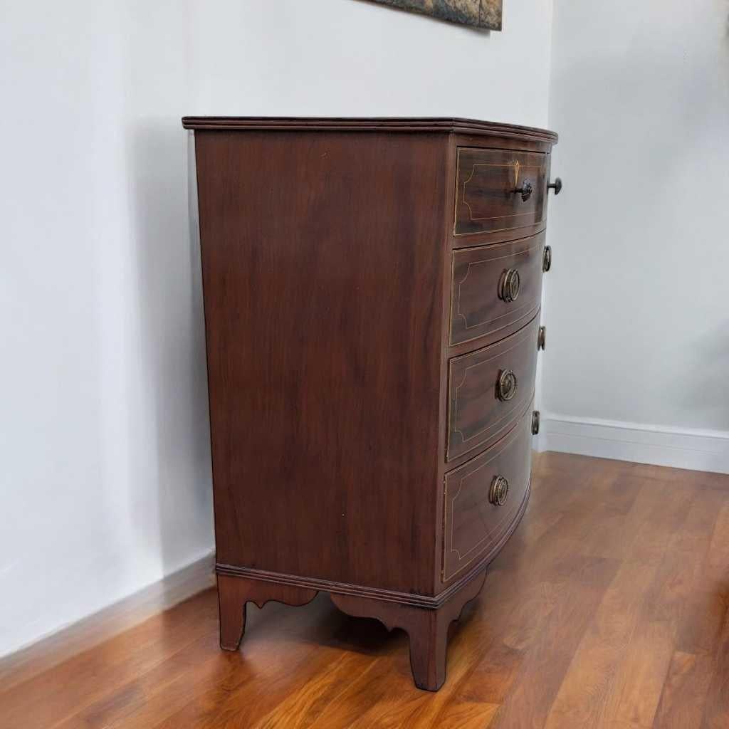 Une commode originale dans la tradition anglaise du début du 20e siècle, fabriquée en placage d'acajou et présentant une façade légèrement incurvée, des proportions classiques et d'élégantes ferrures en laiton d'époque. Cette pièce allie le charme