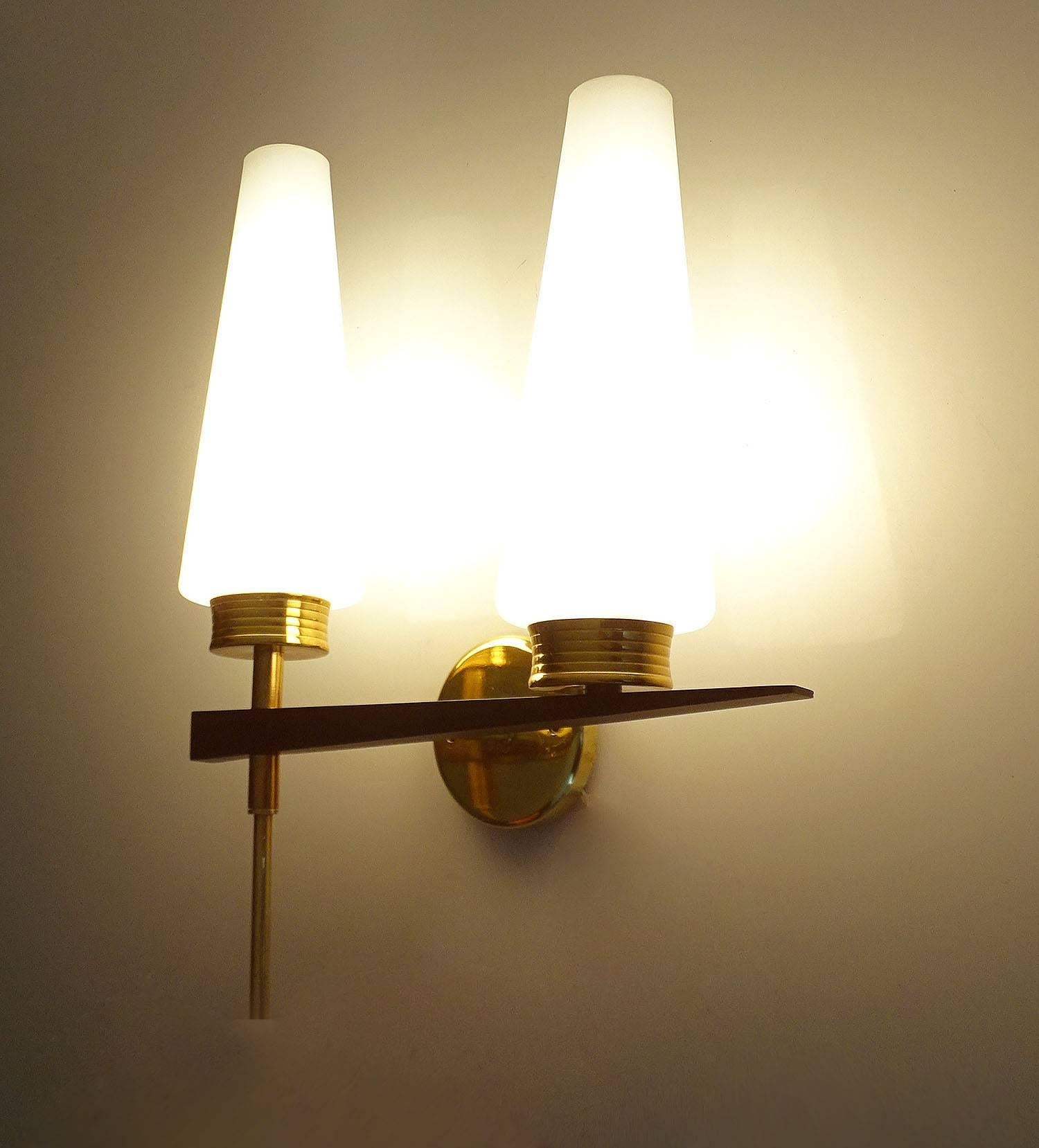 Exceptional pair of  French, architectonic modernist sconces by Maison Arlus, 1960s featuring two conical opaline glass shades mounted on an asymetrical brass and black enameled structure. EWhen lit the sconces exude a warm glow to create a nice