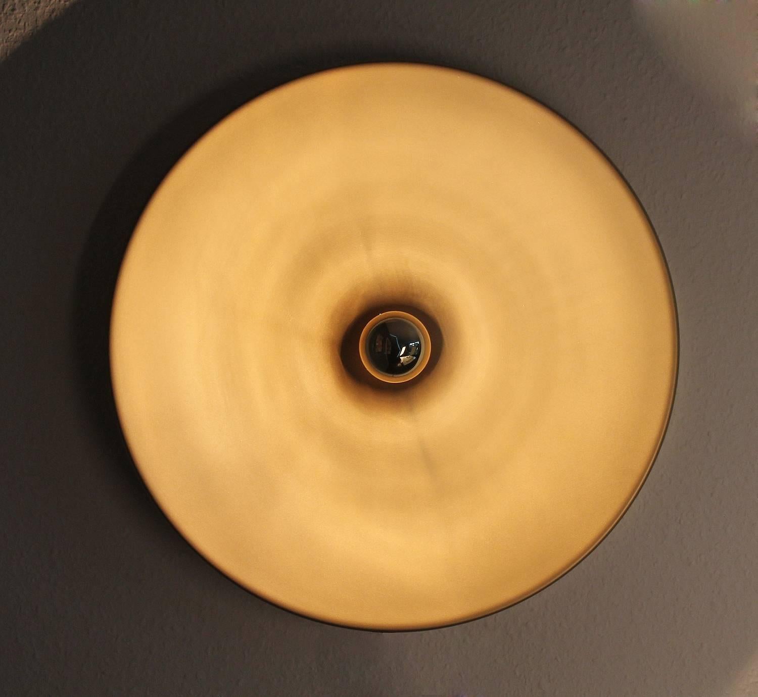 Pair of very large bronze enameled disc shaped sconces in the style of Stilnovo, beautiful minimalistic statement with a smooth lighting effect - best used with a mirrored tip bulb. 
Please note that the wall attachments are different for both