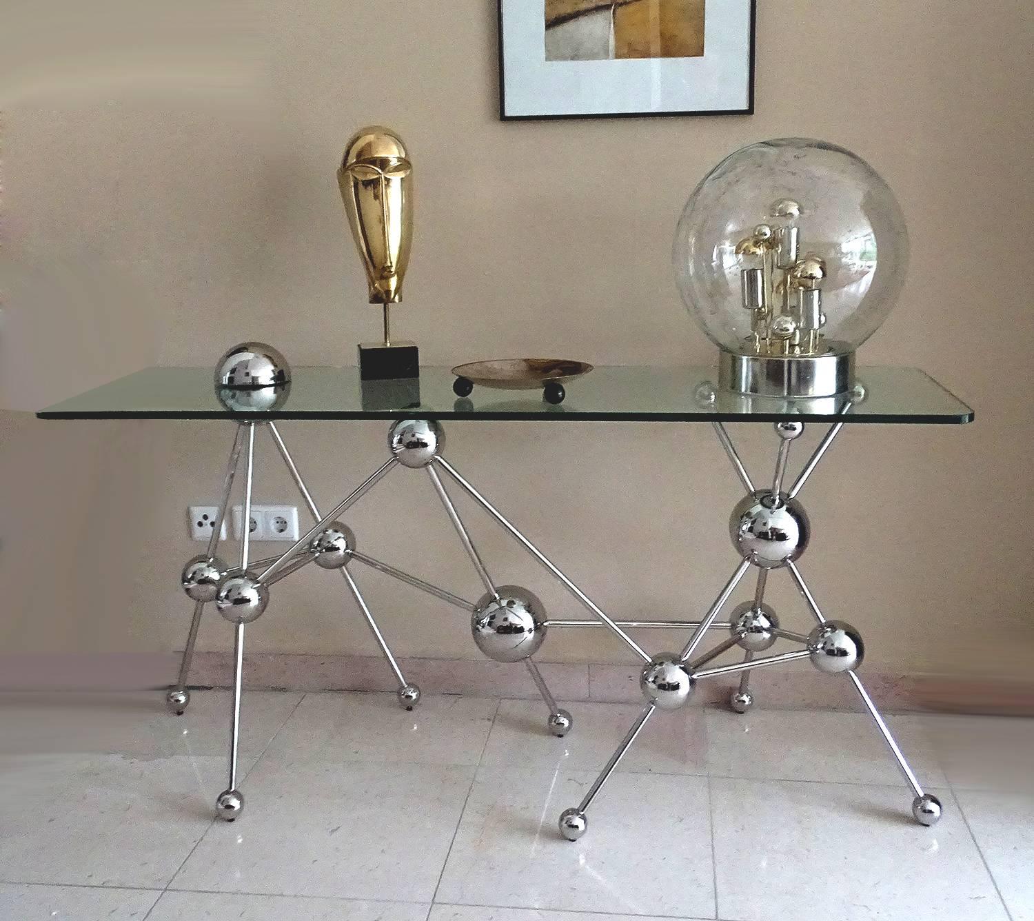 Sculptural console featuring an elaborate frame of assorted diameter spheres connected by slim rods. A glass top reveals the intricate design beneath from any angle. One sphere transcends the glass boundary, connecting the design as one harmonious