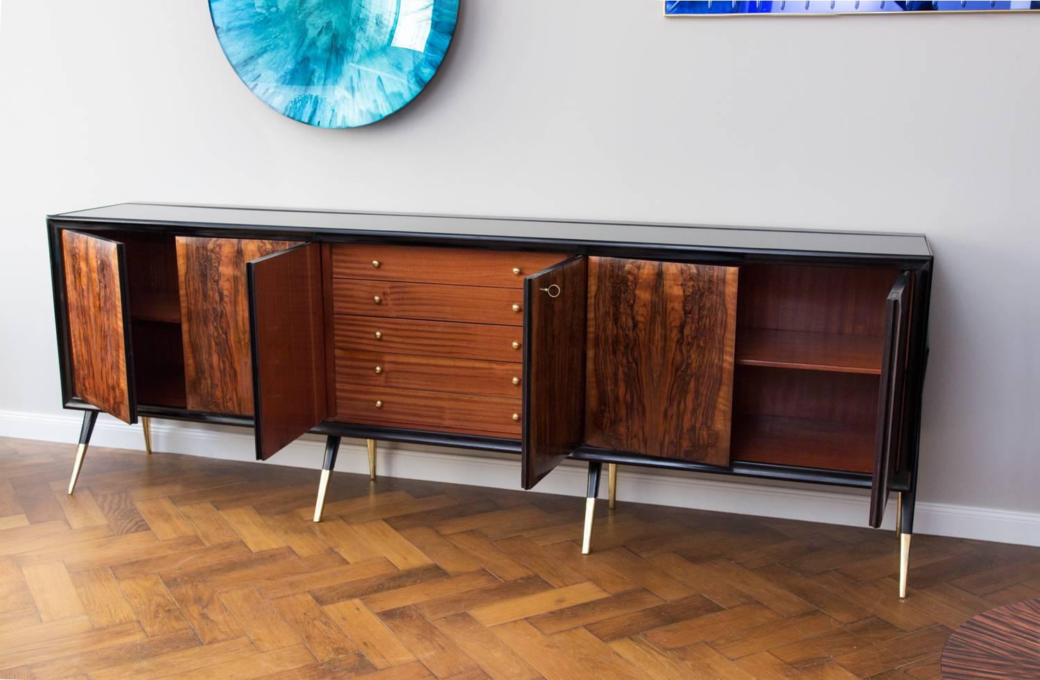 Gigant Sideboard, Italy circa 1950, elegant eight brass legs. Front doors, walnut veneered, shellac polished side legs and frame, black glass top, divided into three compartments. Middle cupboard with five drawers. the sides are veneered rosewood.