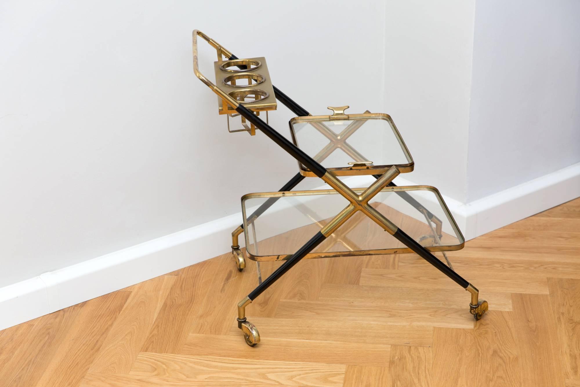 Bar cart by Cesare Lacca, Italy, circa 1950, brass and black polished shellack wood bar cart, tapering sculptural form with two tapering glass tiers, bottle holder, brass rolls. Restored condition with brass patina.