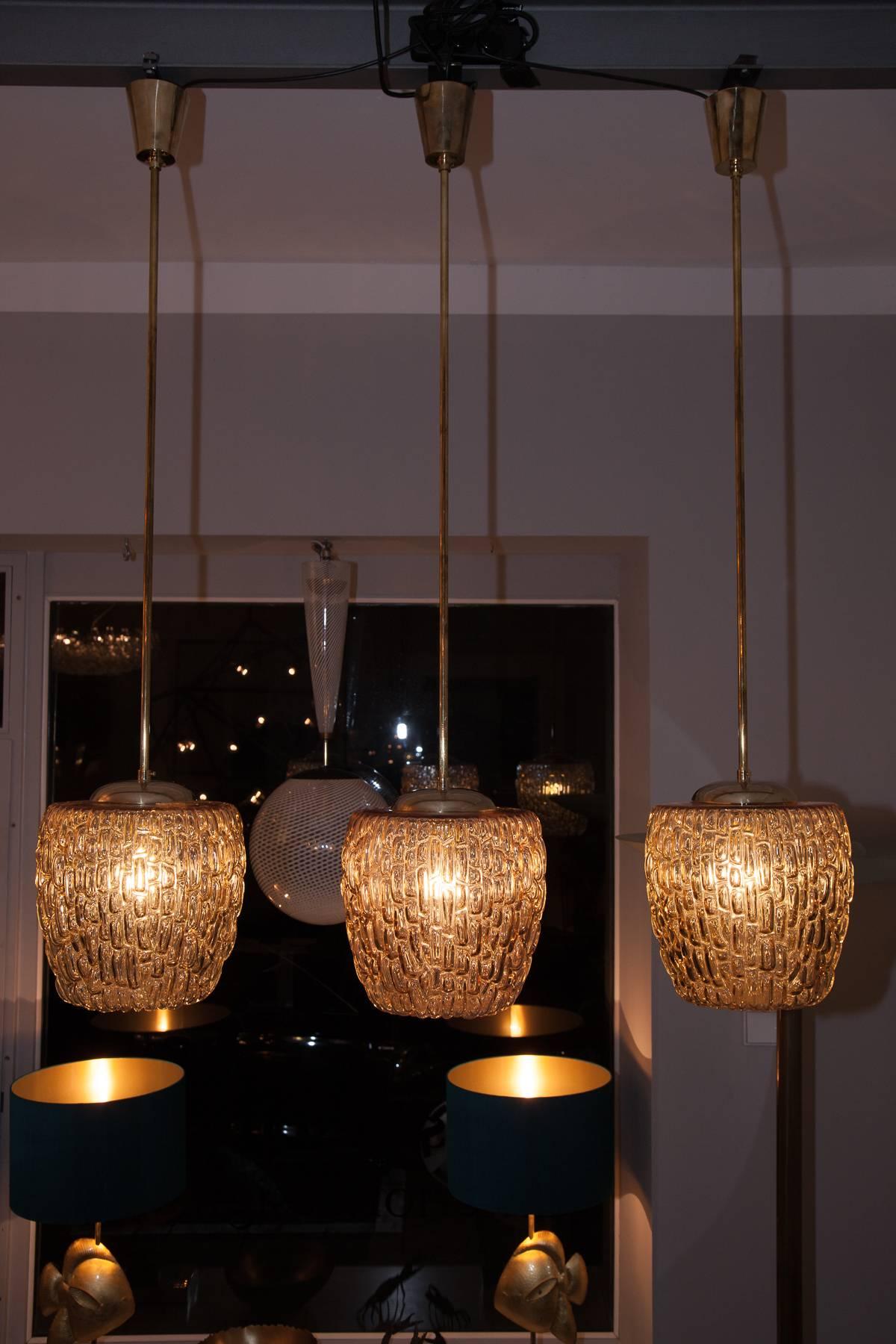 Very unique Austrian Mid-Century set of three ceiling lamps by Rupert Nikoll, Vienna, circa 1950. Orange colored glass body, base suspension, brass rod, heavy brass canopy, brass E27 sockets, rewired. Perfect condition, no scratches or chips in the
