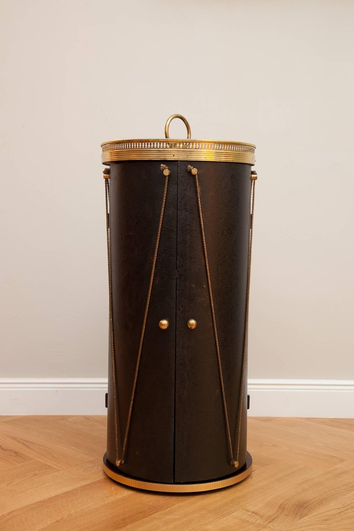 Small bar in form of a drum, Italy circa 1960, two doors, black lacquered metal, gild cords, punched out brass frame, rosewood veneer, brass handle. 
Measures: Height 78 cm, diameter 32 cm.
Perfect condition.