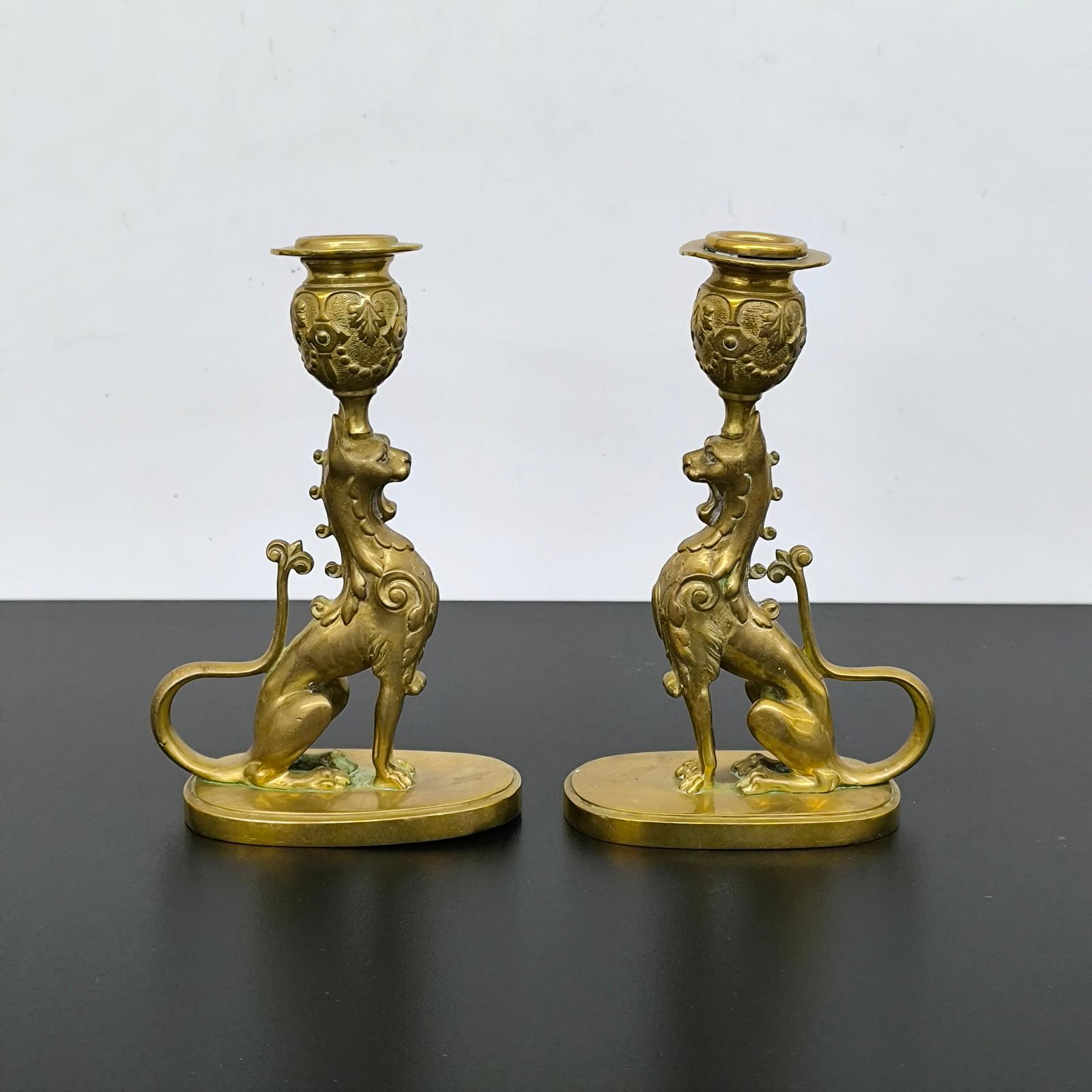 Coppia di candelieri in bronzo dorato raffiguranti due grifoni seduti che tengono in testa un bobeche che forma la torcia. Sono posati su una base ovale, con un marchio di fonderia impresso sotto la base.
Dimensioni: (LxPxA) 10,5 x 6 x 17,5 cm
Buone