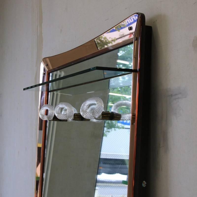 Large floor mirror with glass coat hangers, Italy 1950s.

Large mirror with light pink colored mirror surround, glass shelf and four coat hangers made of turned glass. Brass detail and wooden base. Wonderful!