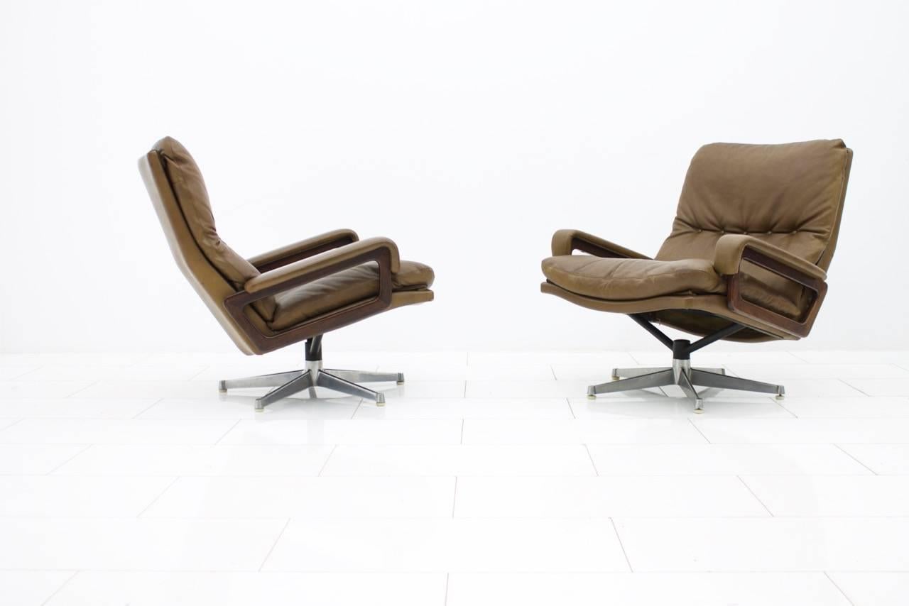 Beautiful and very comfortable set of two swivel lounge chairs in brown leather, metal base and wood armrests. Designed by André Vandenbeuck in 1965 and made by Strässle, Switzerland.
Good original condition.

Measurements in cm.

Lounge chairs W 81