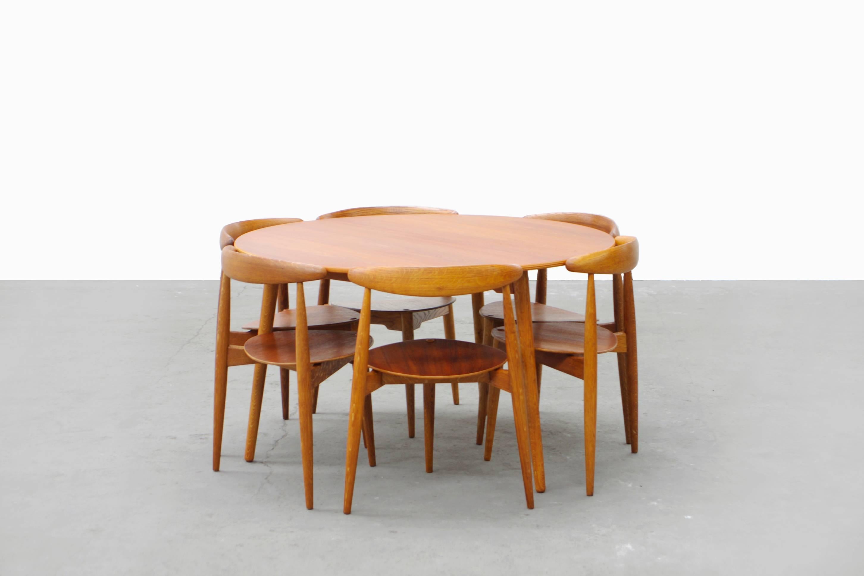 Rare six person dining table set designed for Fritz Hansen by Hans Wegner. Created of both teak and oakwood, the unique design perfectly encapsulates all three-legged chairs under the round table top. The entire group in is great condition with