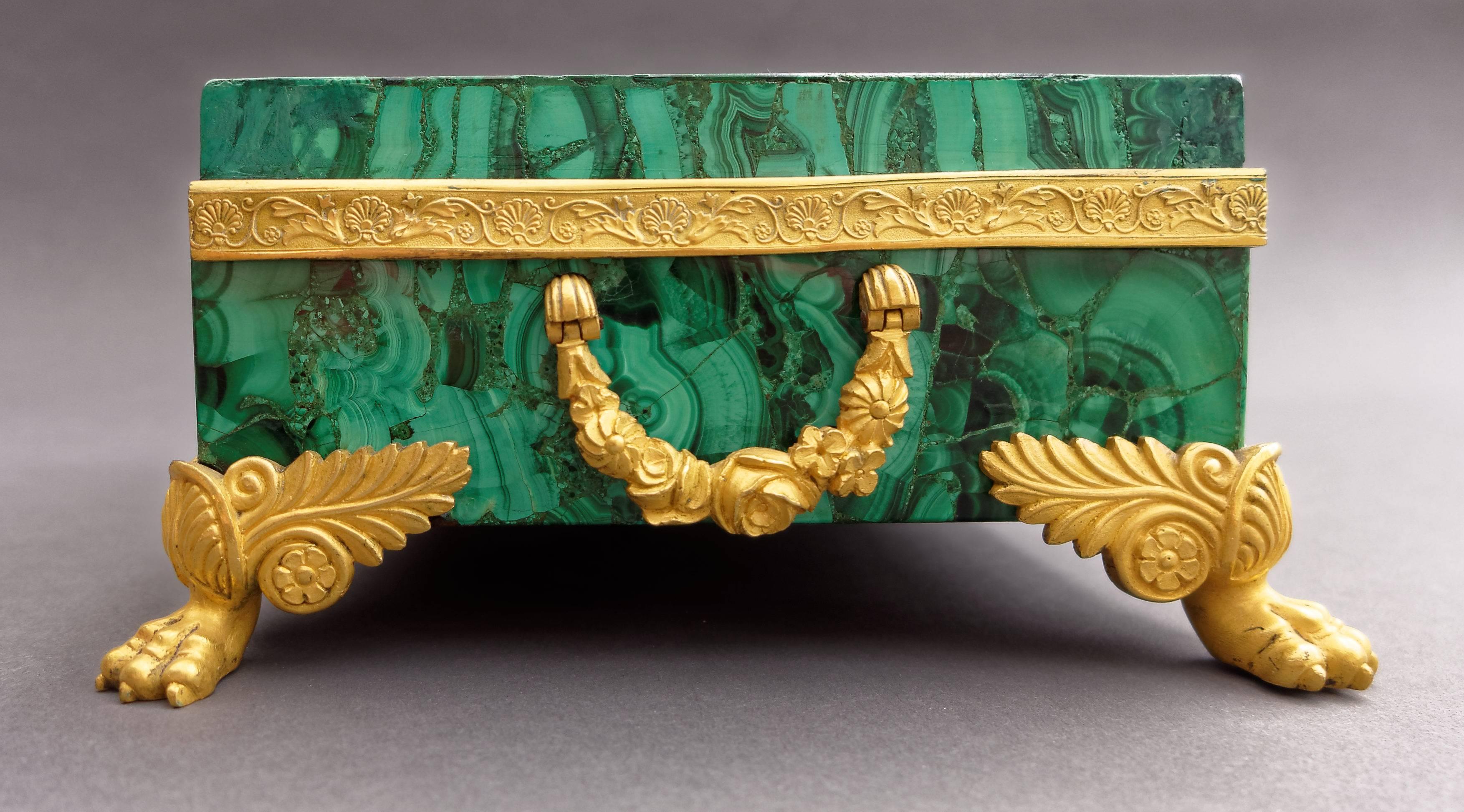 A very fine Russian giltbronze mounted malachite veneered box from the first quarter of the 19th century. Of rectangular form with hinged lid, supported on four paw feet decorated with scrolling acanthus leaves; two flower decorated handles on the