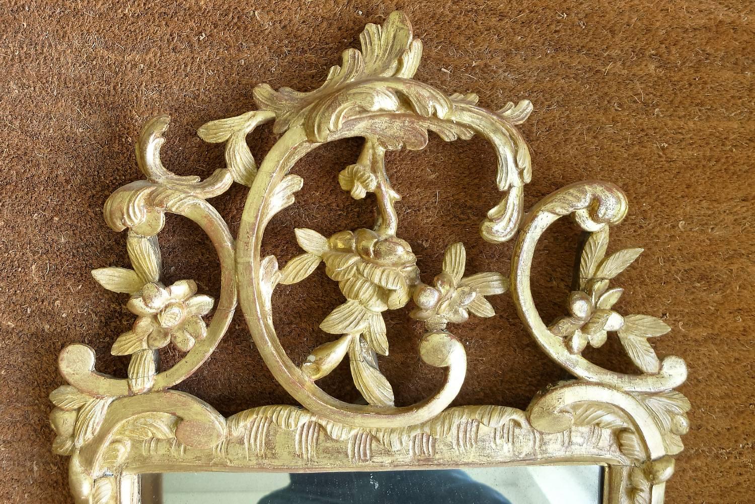 The rectangular plate within a moulded frame carved with flower heads, surmounted by an elaborate pierced C-scroll cresting.