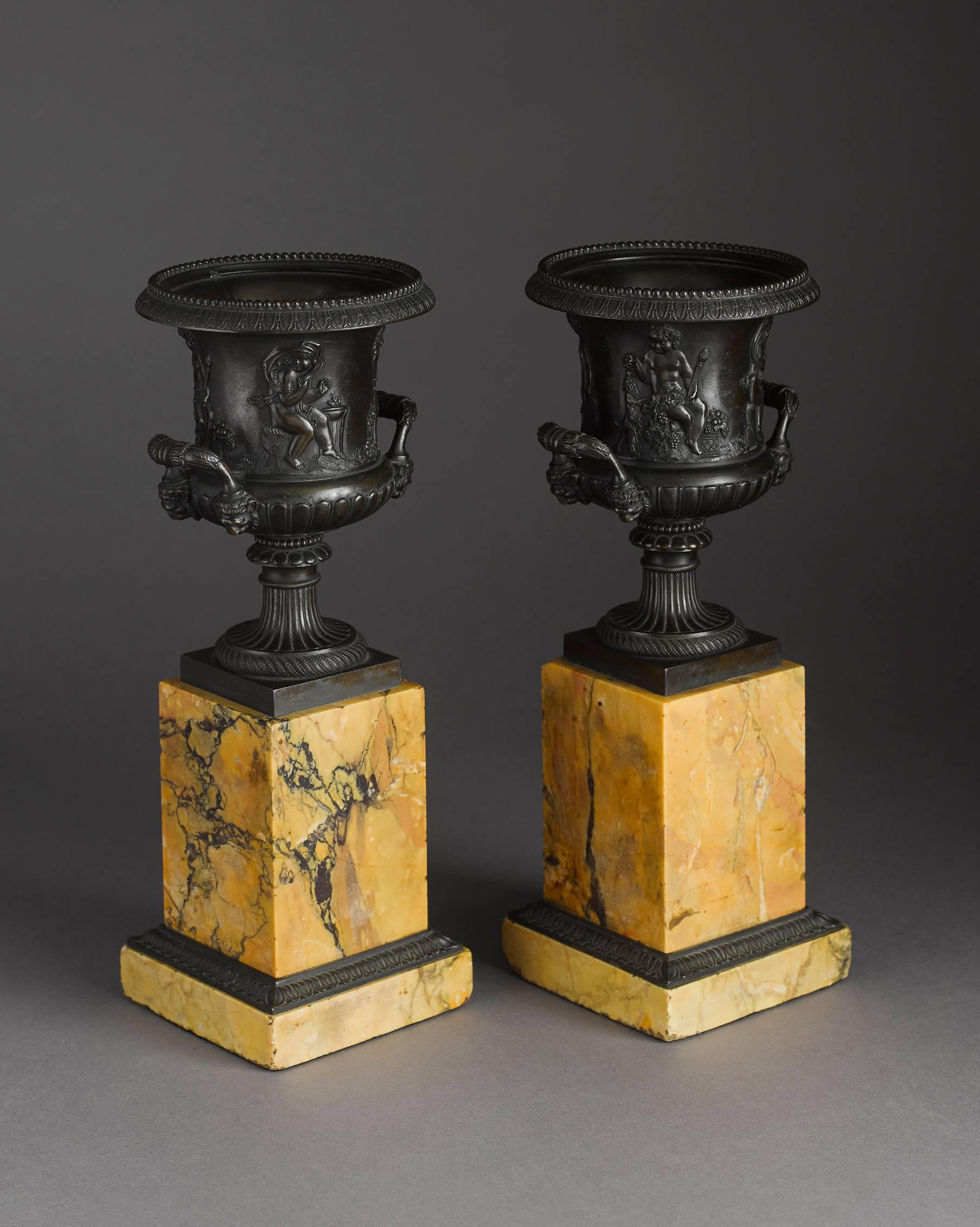 A fine pair of early to mid-19th century Campana shaped patinated bronze urns on Sienna marble pedestals. The bronzes are of good quality with fine ciseling, the handles with lion heads, the body with a frieze of four sitting putti symolizing the