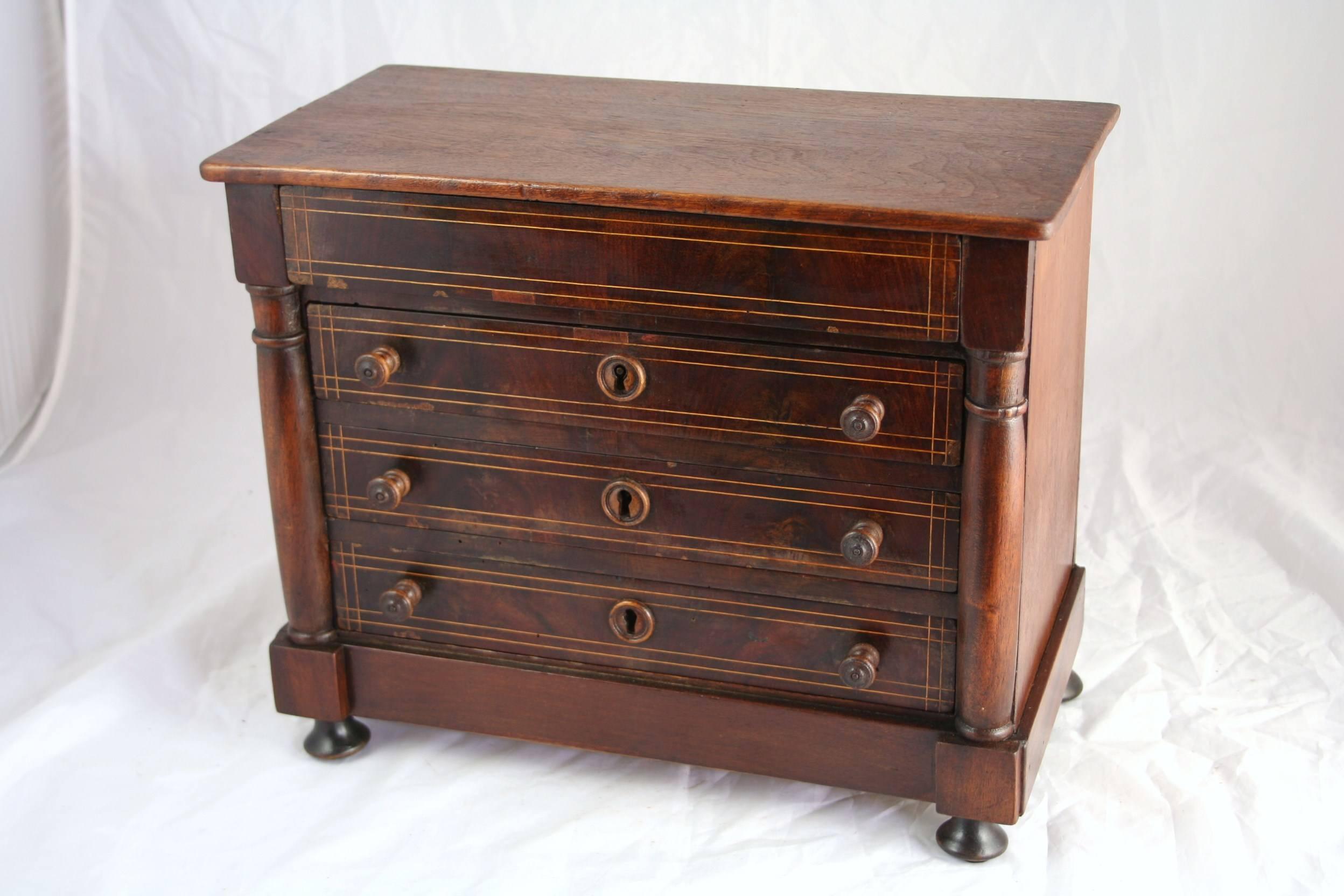 This fantastic 19th century Charles X style miniature chest features beautifully burled deeply toned walnut with lemon wood inlay. Accented with Empire columns, this piece has three drawers with pulls and original wooden key entries. A fourth top