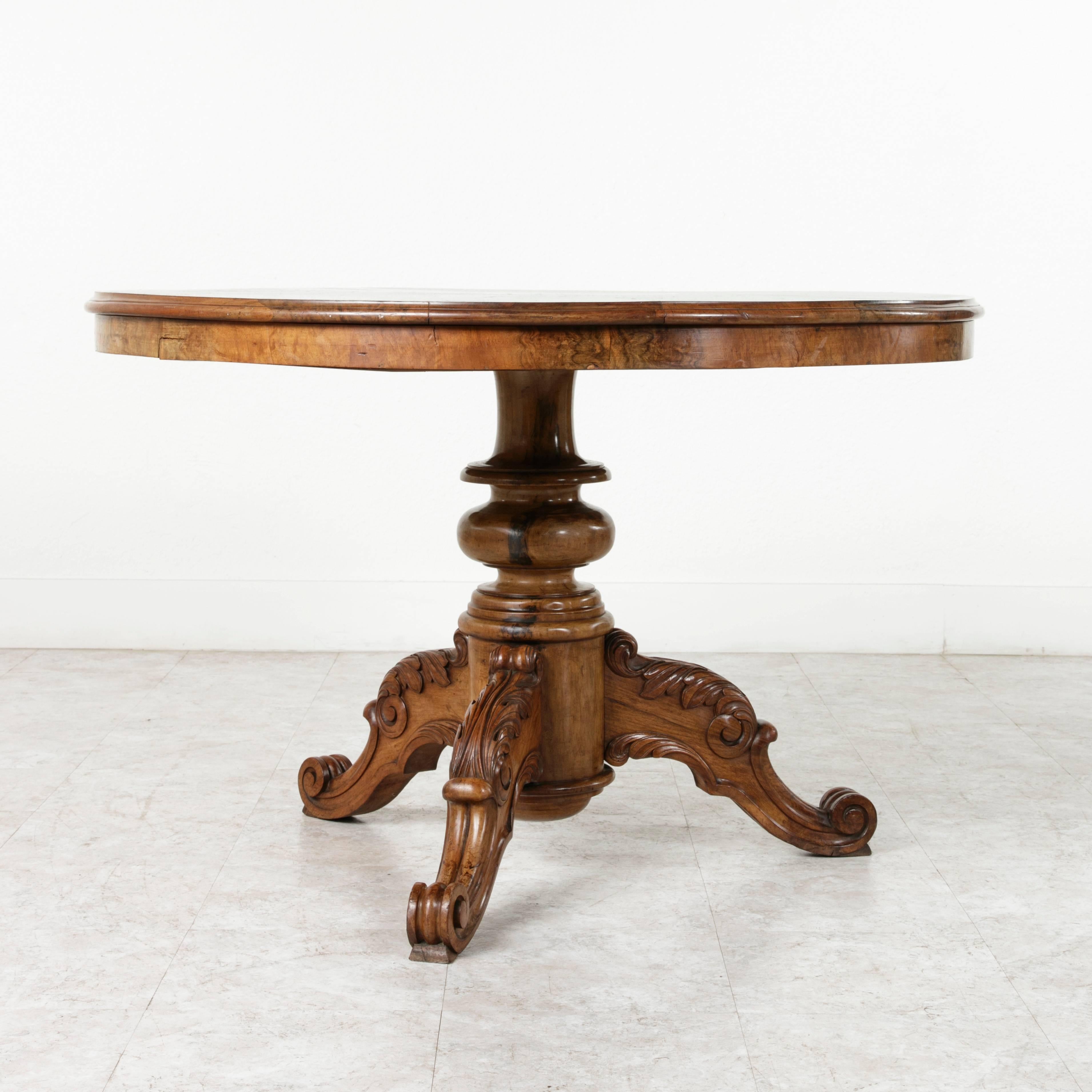 This Restauration period center table features a top of burled walnut perfectly book matched to create a seven point star. Its solid walnut pedestal base is intricately hand carved with scrolling acanthus. A simple latch can be turned to release and