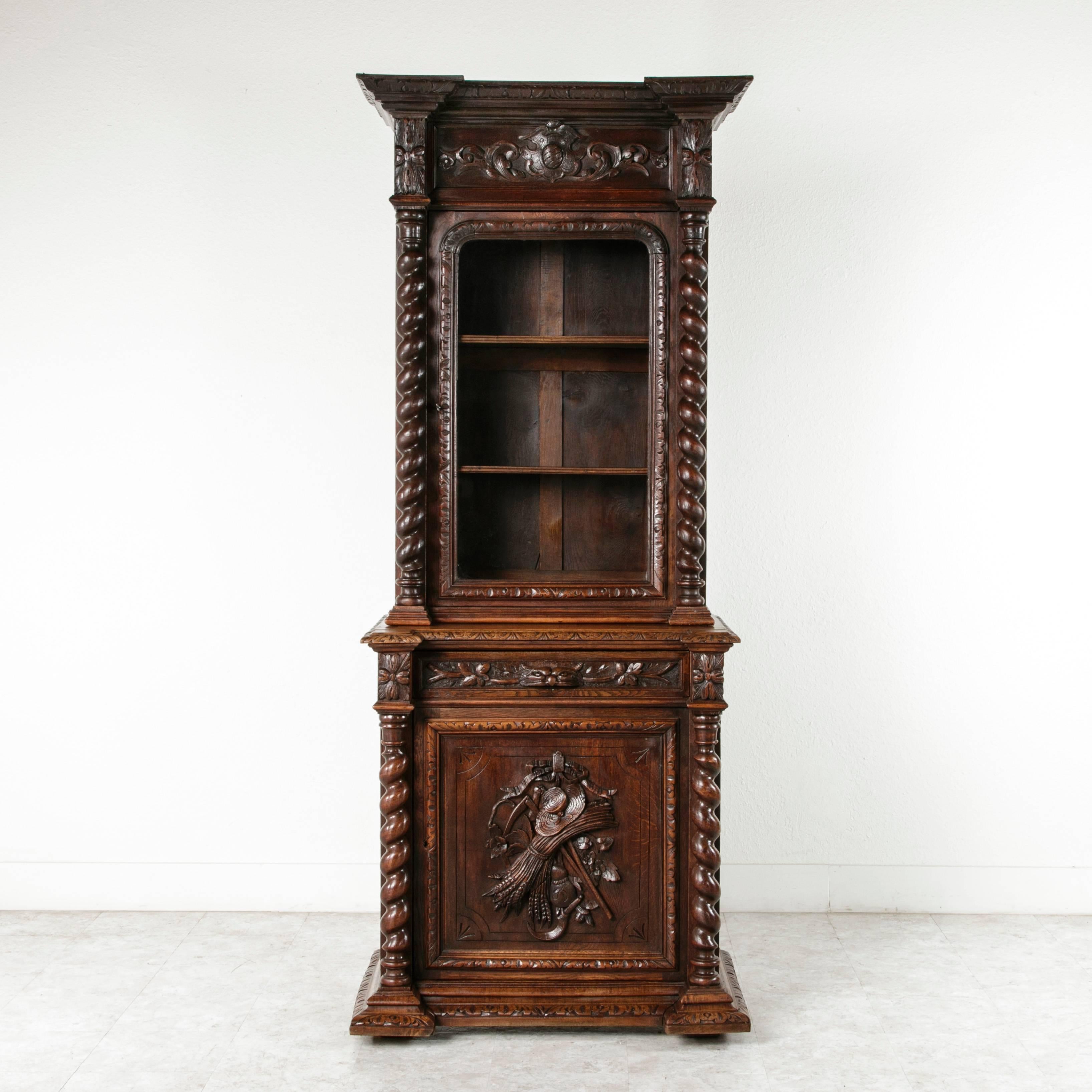 This beautifully hand-carved oak Louis XIII style buffet deux corps features barley twist columns, single door, and single drawer. The carvings on the lower door include an unusual motif of garden attributes with hat, scythe, and sheaves of wheat