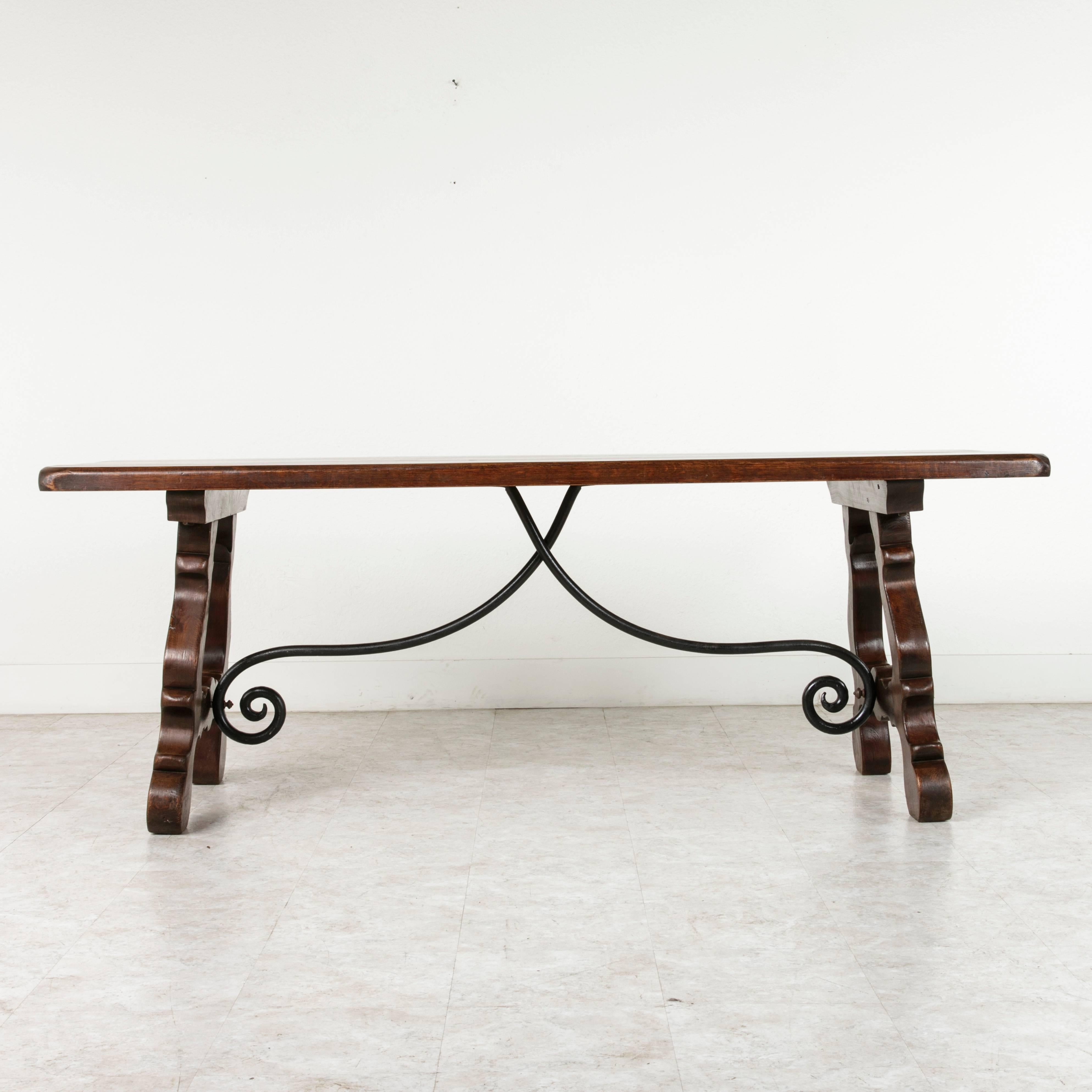 This beautifully carved Spanish Renaissance style dining, console or sofa table features a hand-forged wrought iron trestle support. Its thick solid oak construction and dark patina give it a handsome old world feel, while its carved legs and light