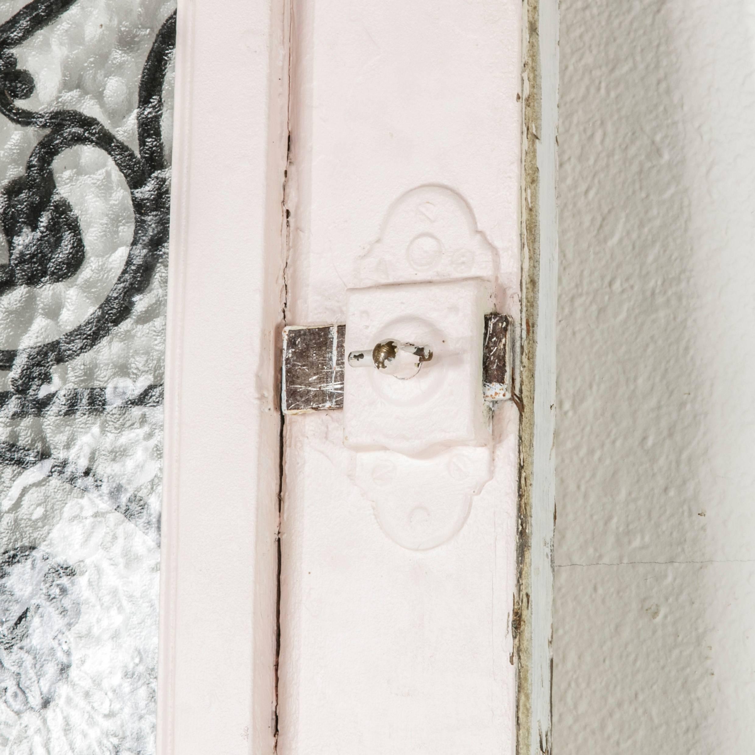 This solid oak painted entry door features two cast iron Art Nouveau period window grills inset behind hinged glass windows that swing open from the inside, allowing for a breeze of fresh air. This door has an iron lock that latches from the inside