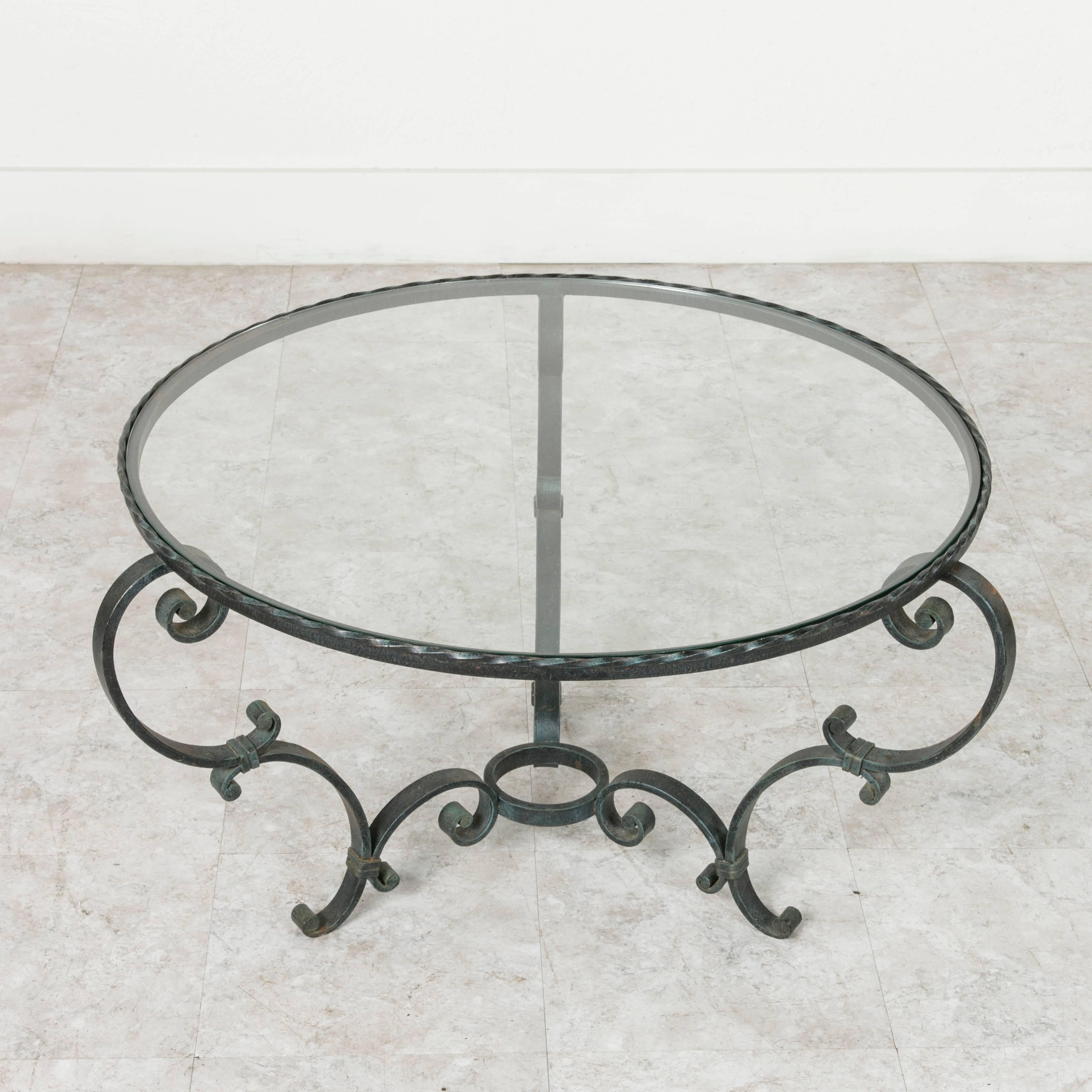 This glass topped round wrought iron coffee table was made by hand in France in the early 20th century. The circular top is nearly three feet in diameter, making it an excellent scale for most seating areas. The airy curves of this piece are both