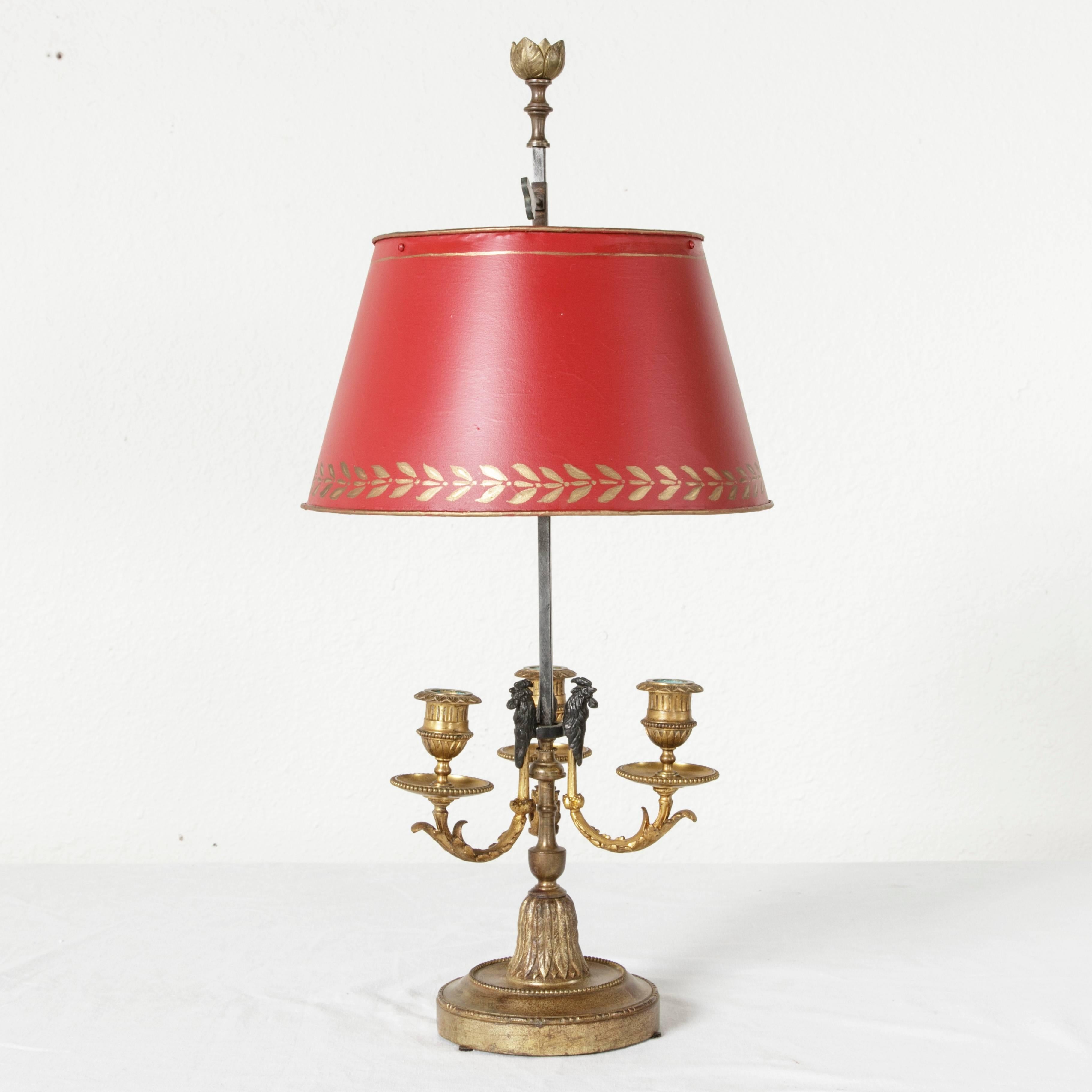 This superb lamp bouillotte features bronze roosters surrounding its central pillar, with an intricate bronze doré base and three arms for candles. The tole painted red and gold shade is on an adjustable square edged column topped with a finial of
