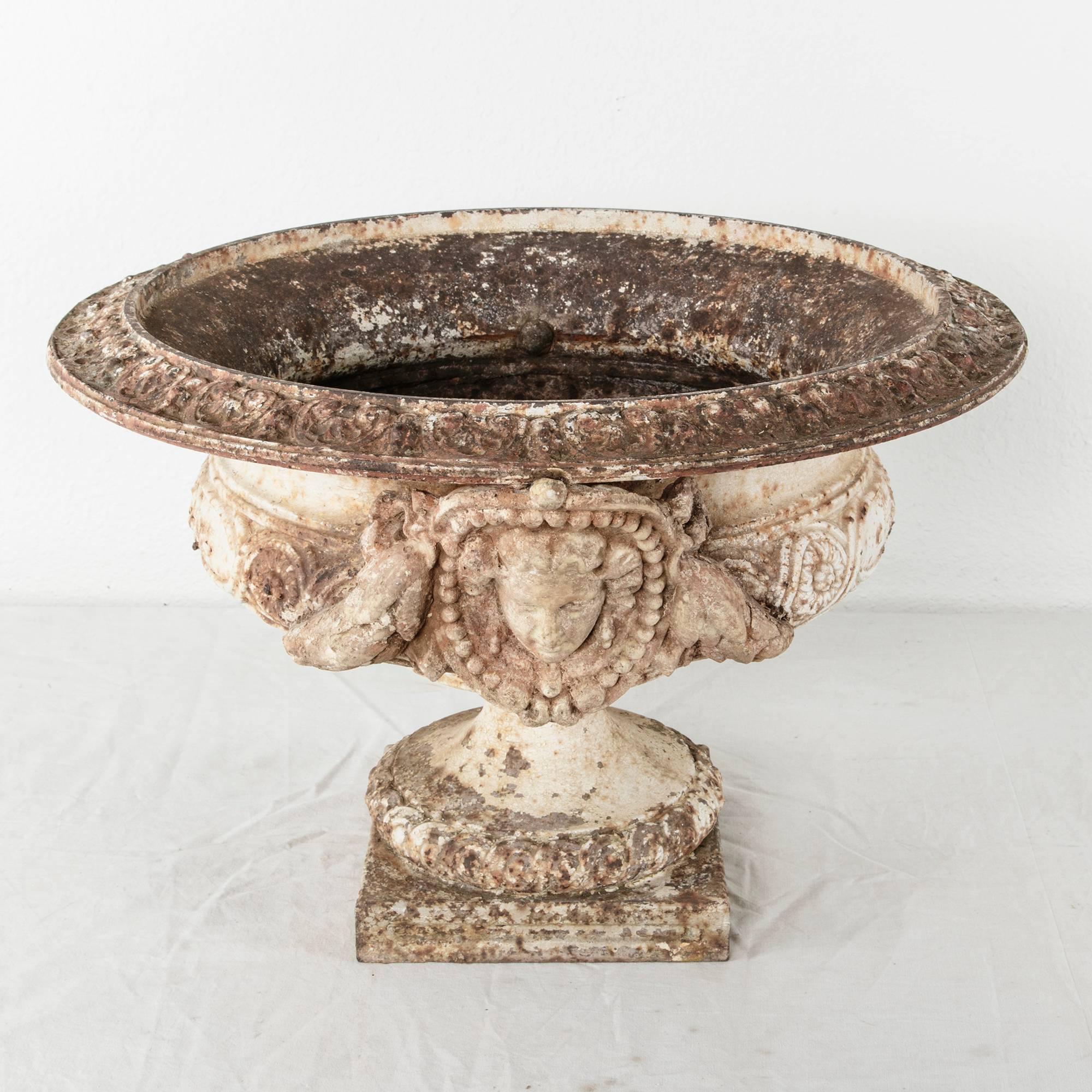 This very large 18th century cast iron garden urn features stone handles of classical female faces. A statement piece for a formal garden or grand entry, this urn is sure to make an impression. A rich patina of lichen and rust tones adds depth and
