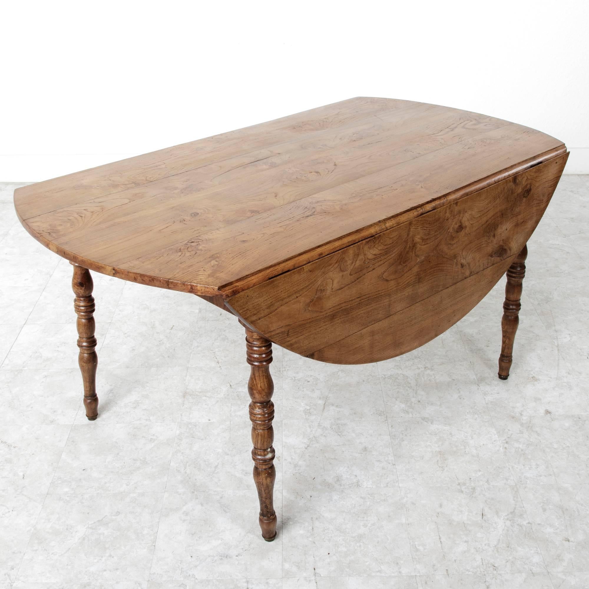 This 19th century French round elm dining table features turned legs and drop leaves. The simple airy profile of this table allows the beauty of its wood to show. An unusually large and sturdy example at nearly 60