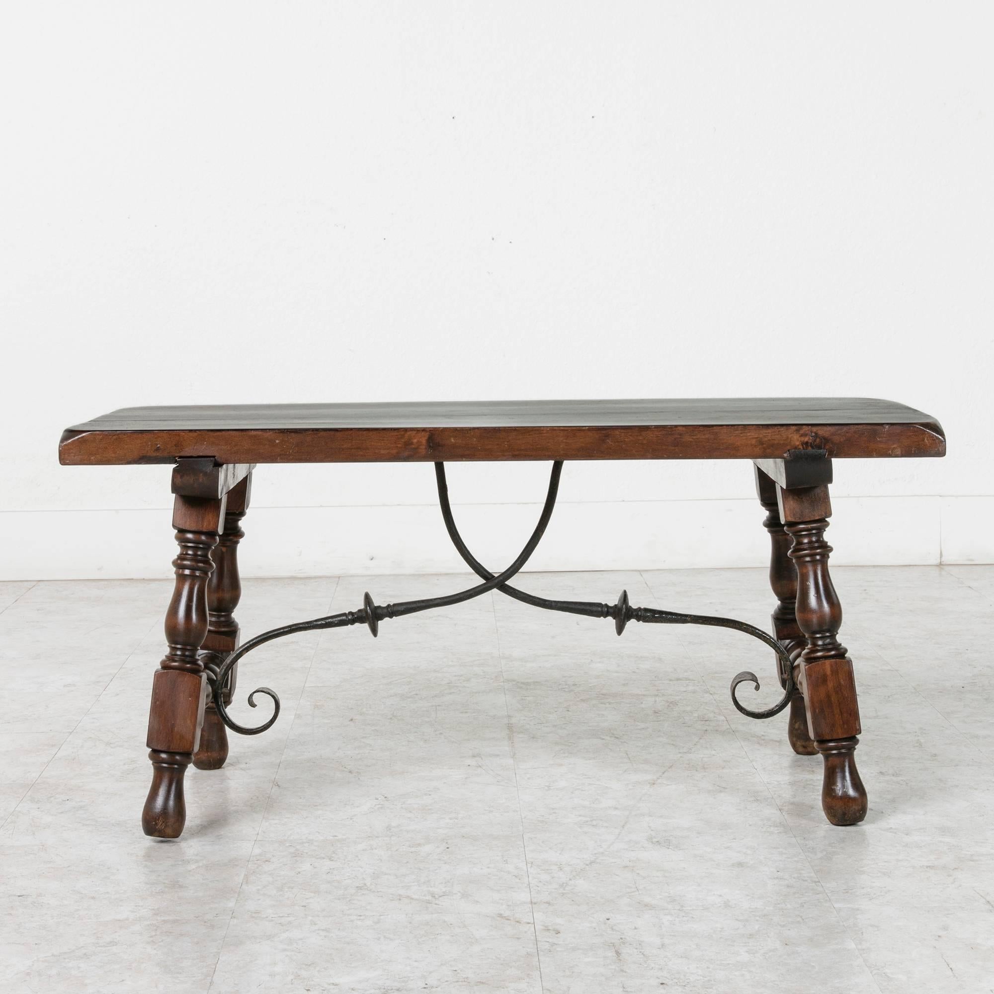 Constructed of solid ash by artisans in the early 20th century, this Spanish Renaissance style coffee table features a hand-forged iron stretcher. Of an excellent versatile scale, this coffee table will make a style statement in a small seating