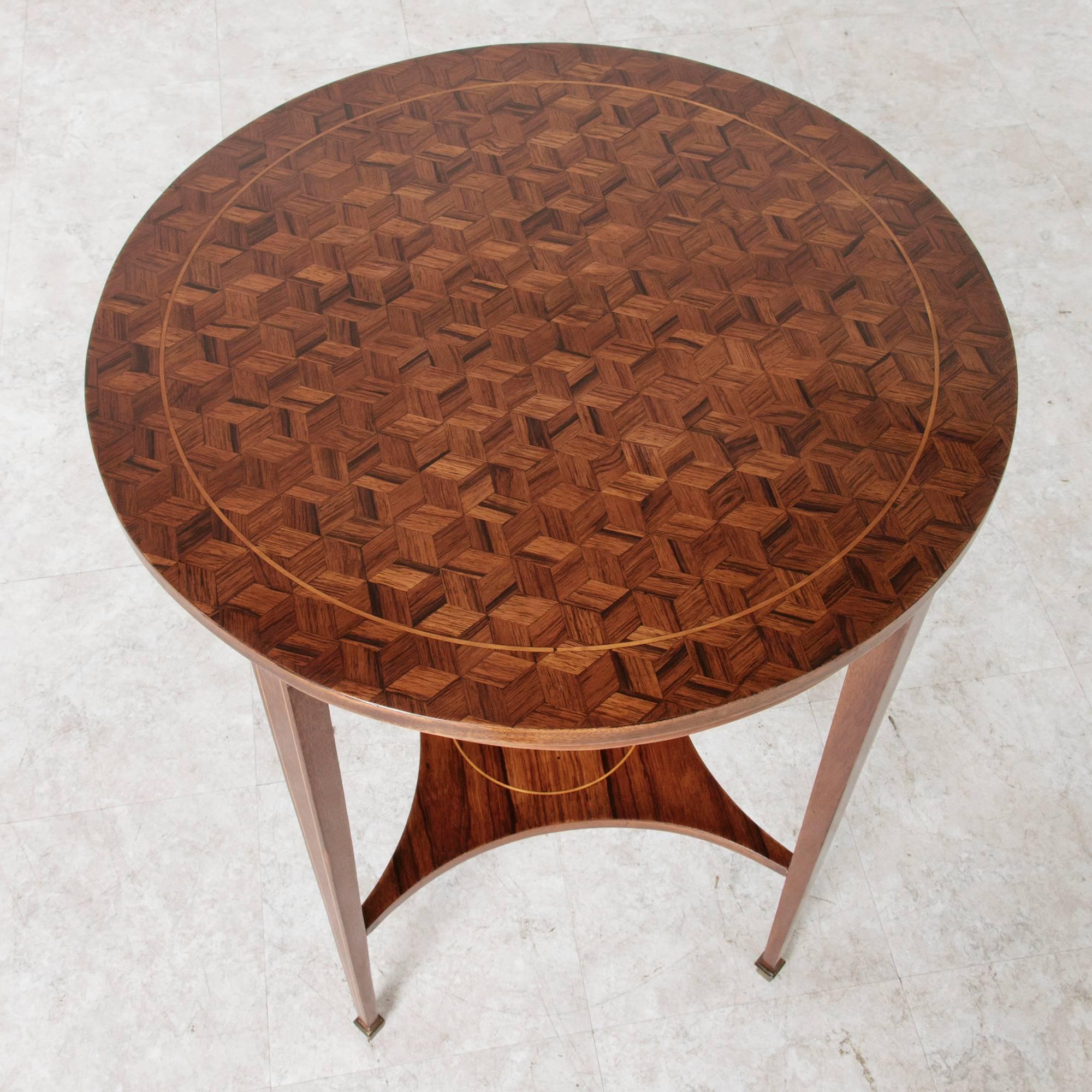This French Art Deco period round side table features a parquetry top of intricate geometric inlay of rosewood accented with a pin line of inlaid lemonwood.  The delicate lemonwood pin line is repeated on its lower shelf and along its tapered legs