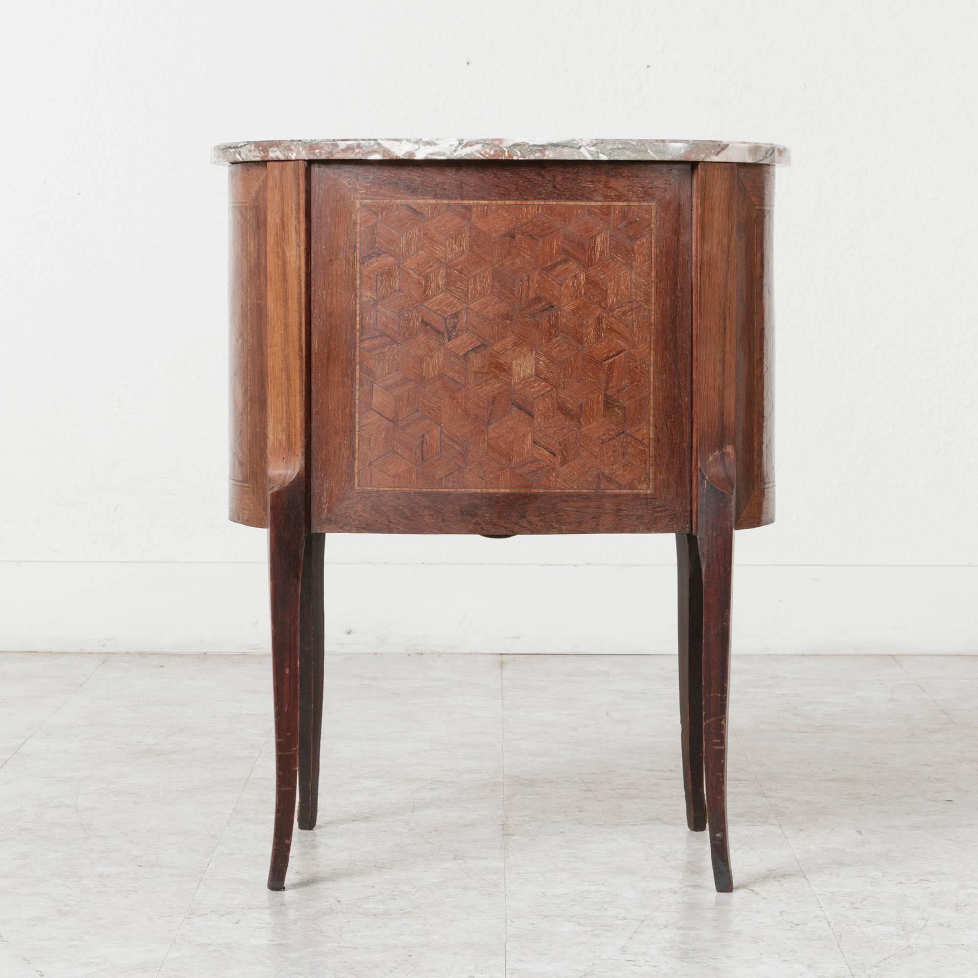 This finely detailed petite commode features a kidney shaped breccia marble top on a conforming case. With inlaid geometric parquetry on all sides and bronze ormolu accents, this small chest will make an elegant nightstand or floating side table.
